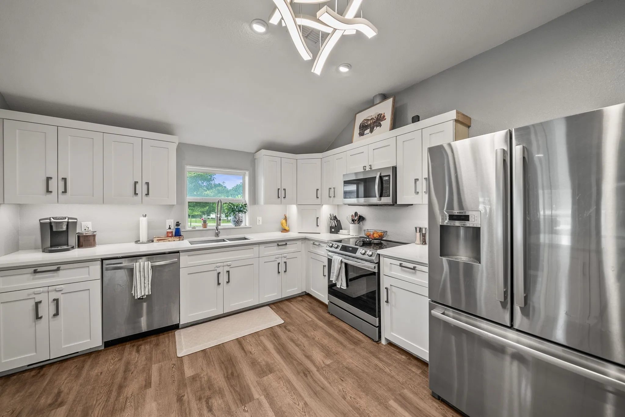 Modern kitchen featuring white shaker cabinetry, stainless steel appliances, wood-finish flooring, recessed lighting, and a contemporary ceiling fixture