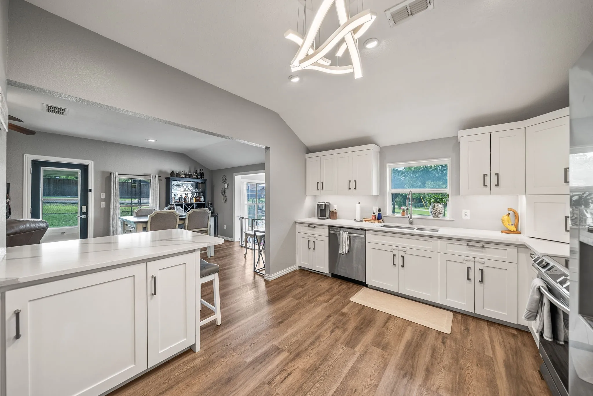 Modern kitchen featuring white shaker cabinetry, stainless steel appliances, light countertops, wood-finish flooring, and a contemporary ceiling light fixture