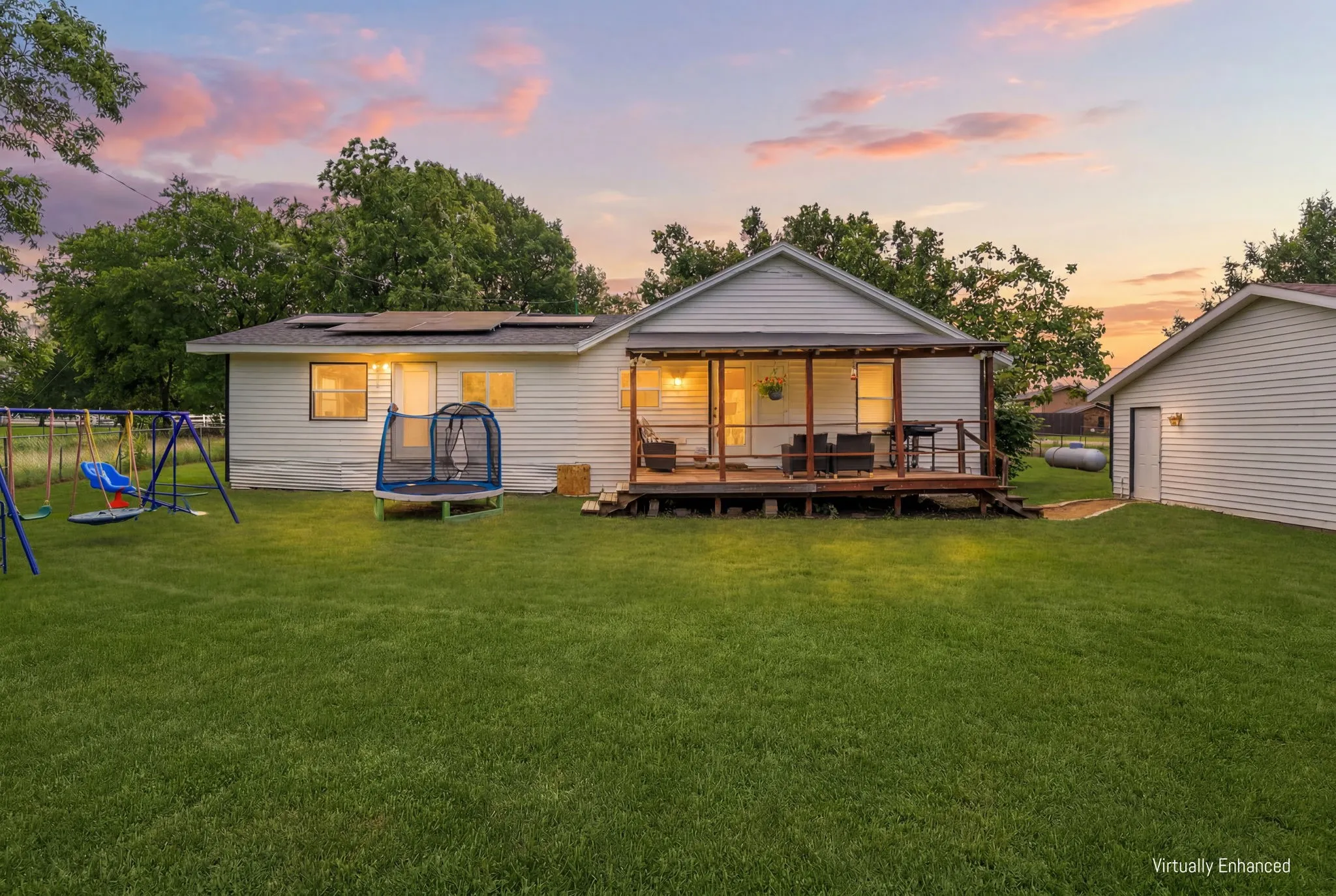 Expansive backyard featuring a wood deck, covered patio, white siding exterior, and a detached structure