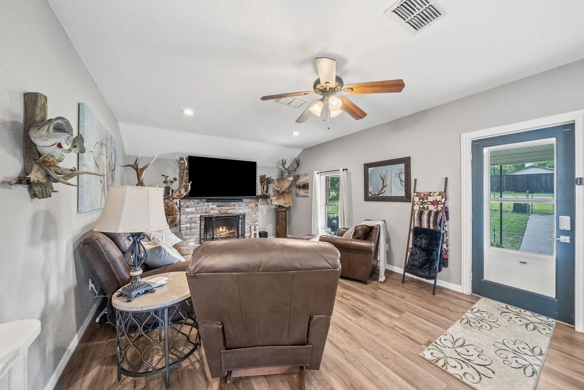 Living room with wood-finish flooring, a stone fireplace, and a ceiling fan