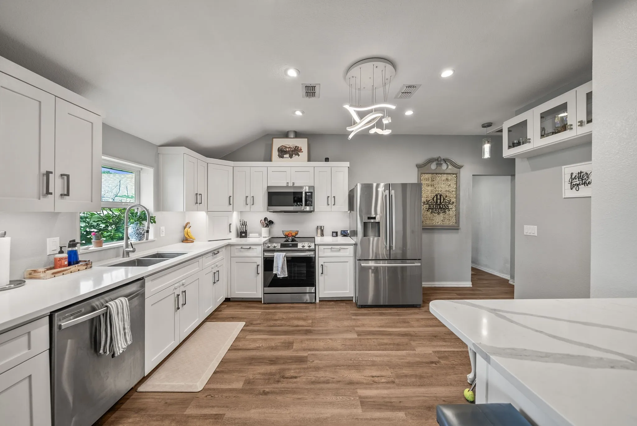 Contemporary kitchen featuring white cabinetry, stainless steel appliances, wood-finish flooring, quartz countertops, and a modern ceiling light fixture
