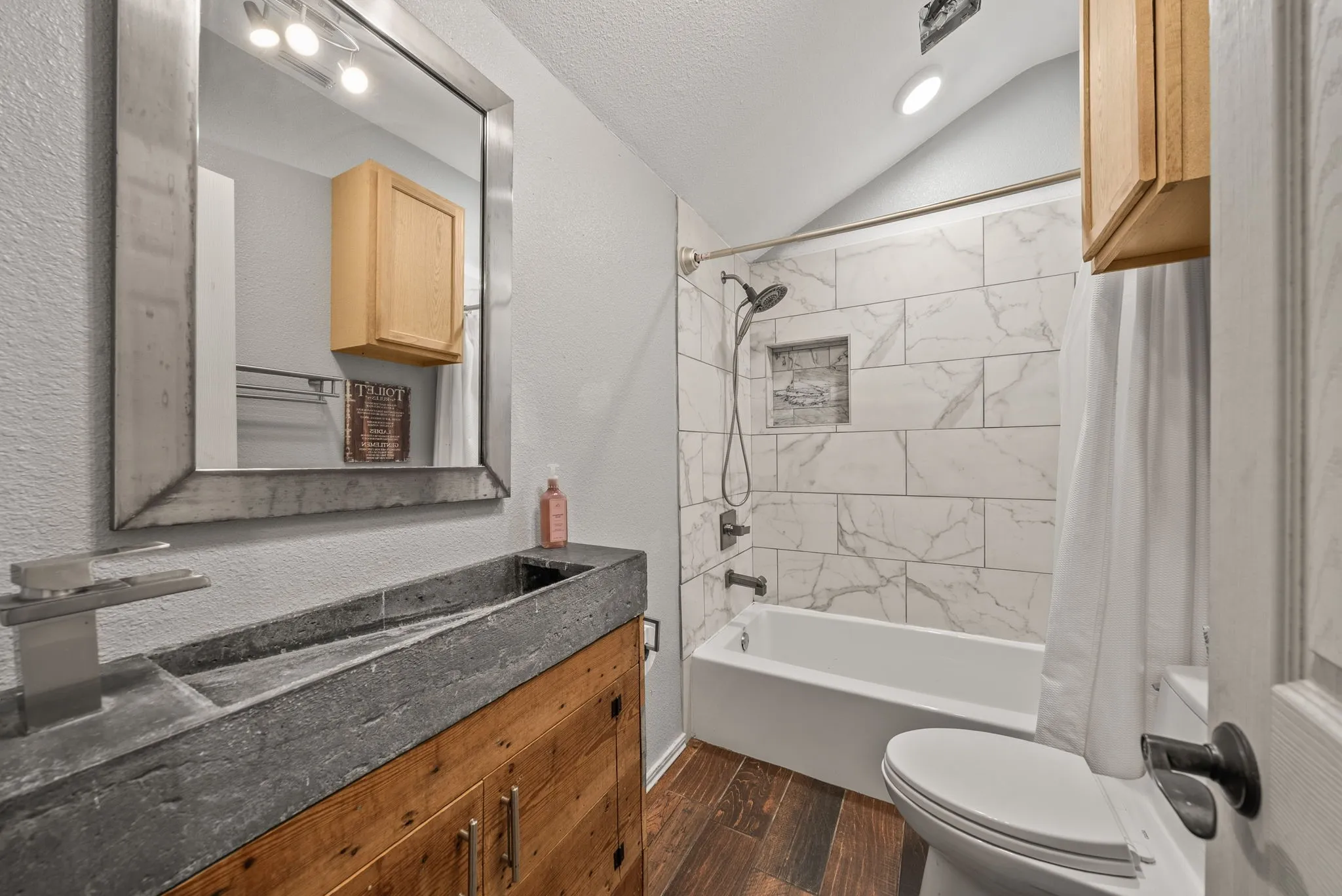 Bathroom featuring a concrete vanity with an integrated sink, wood-finish cabinetry, a framed mirror, and wood-finish flooring