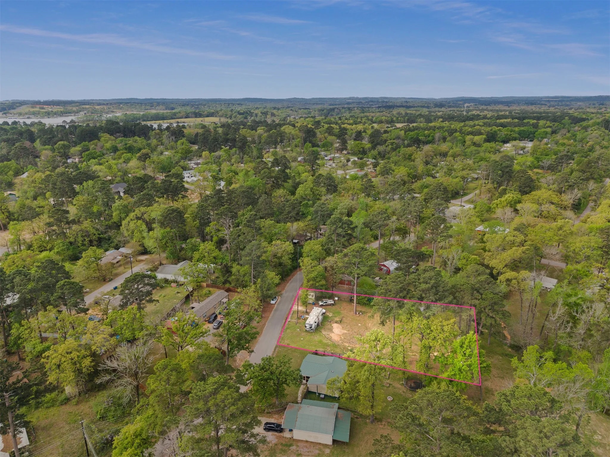 Aerial perspective showcasing a property outlined in pink, featuring ample tree coverage and a paved road frontage
