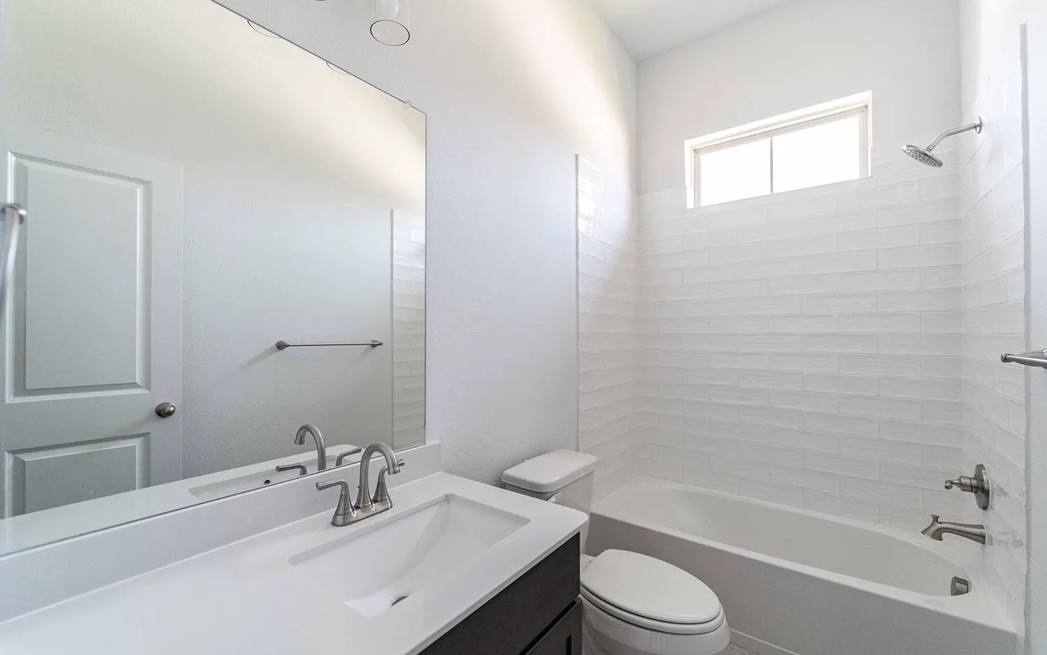 Bathroom featuring a vanity with an integrated sink, brushed nickel faucet, large wall mirror, and a tub-shower combination with horizontal white tile surround