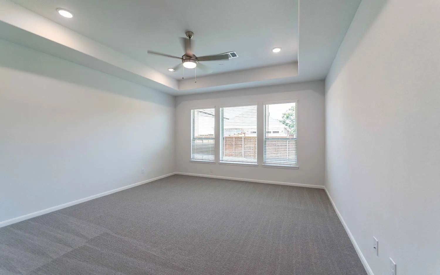 Spacious room featuring a tray ceiling with recessed lighting and a ceiling fan