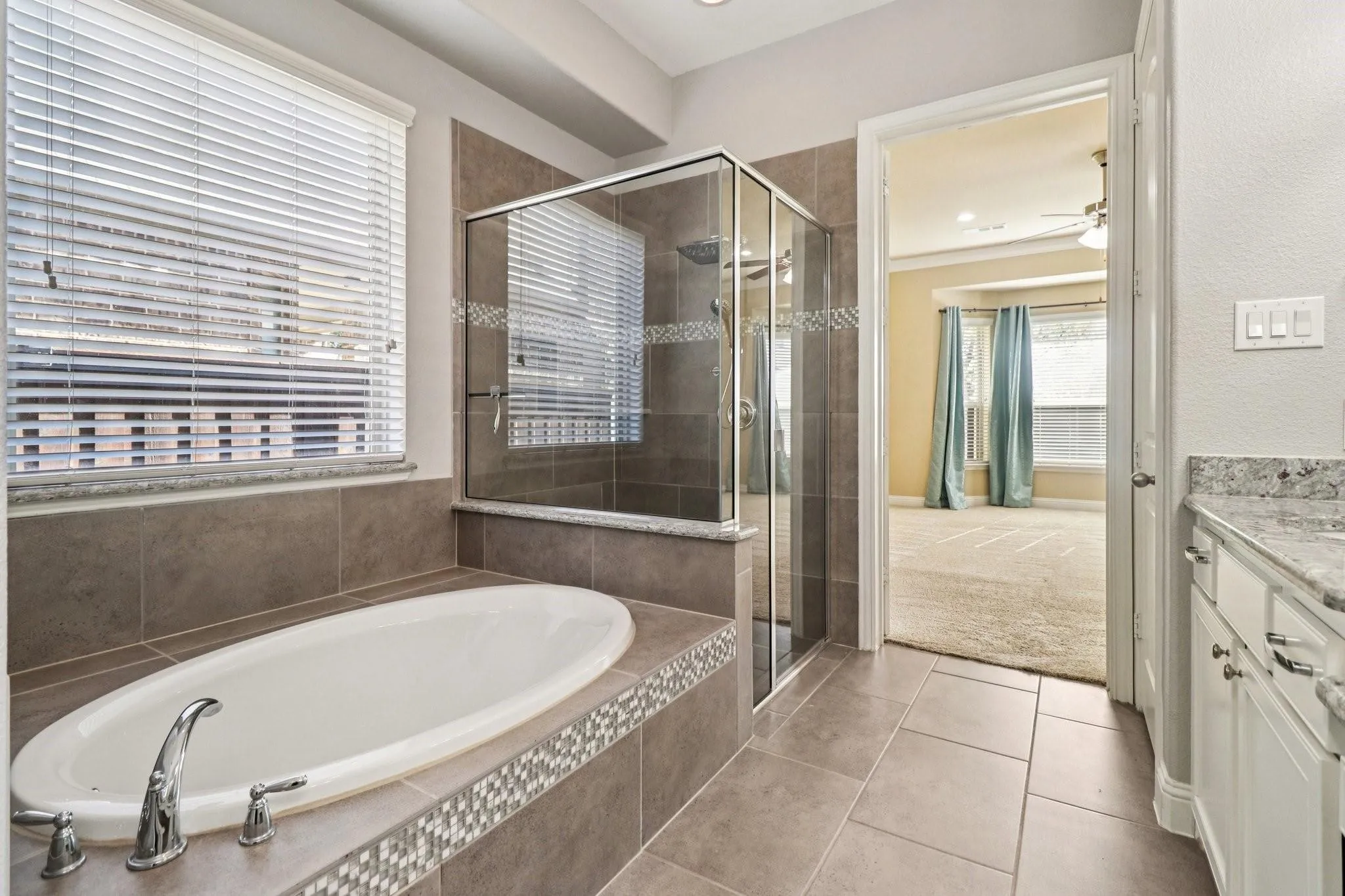 Built-in soaking tub with chrome fixtures, glass-enclosed shower, stone-look tile flooring, and a granite-topped vanity