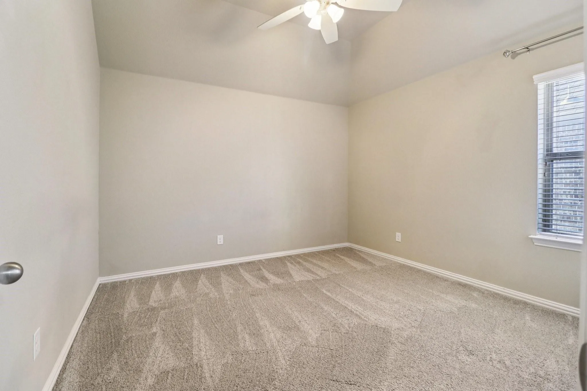 Neutral tone wall paint, vaulted ceiling, ceiling fan with light fixture, window with horizontal blinds, and carpeting