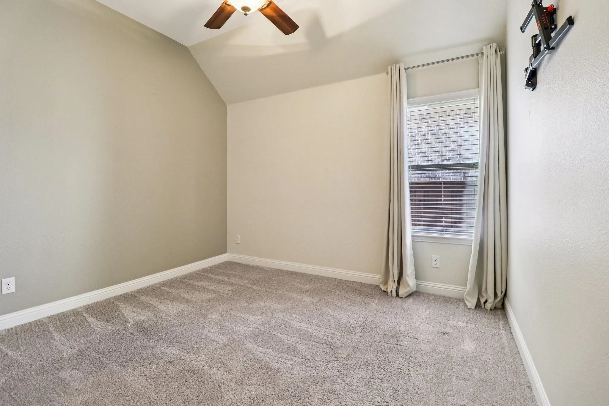 Carpeted room with a vaulted ceiling, ceiling fan, and a window featuring blinds and drapes