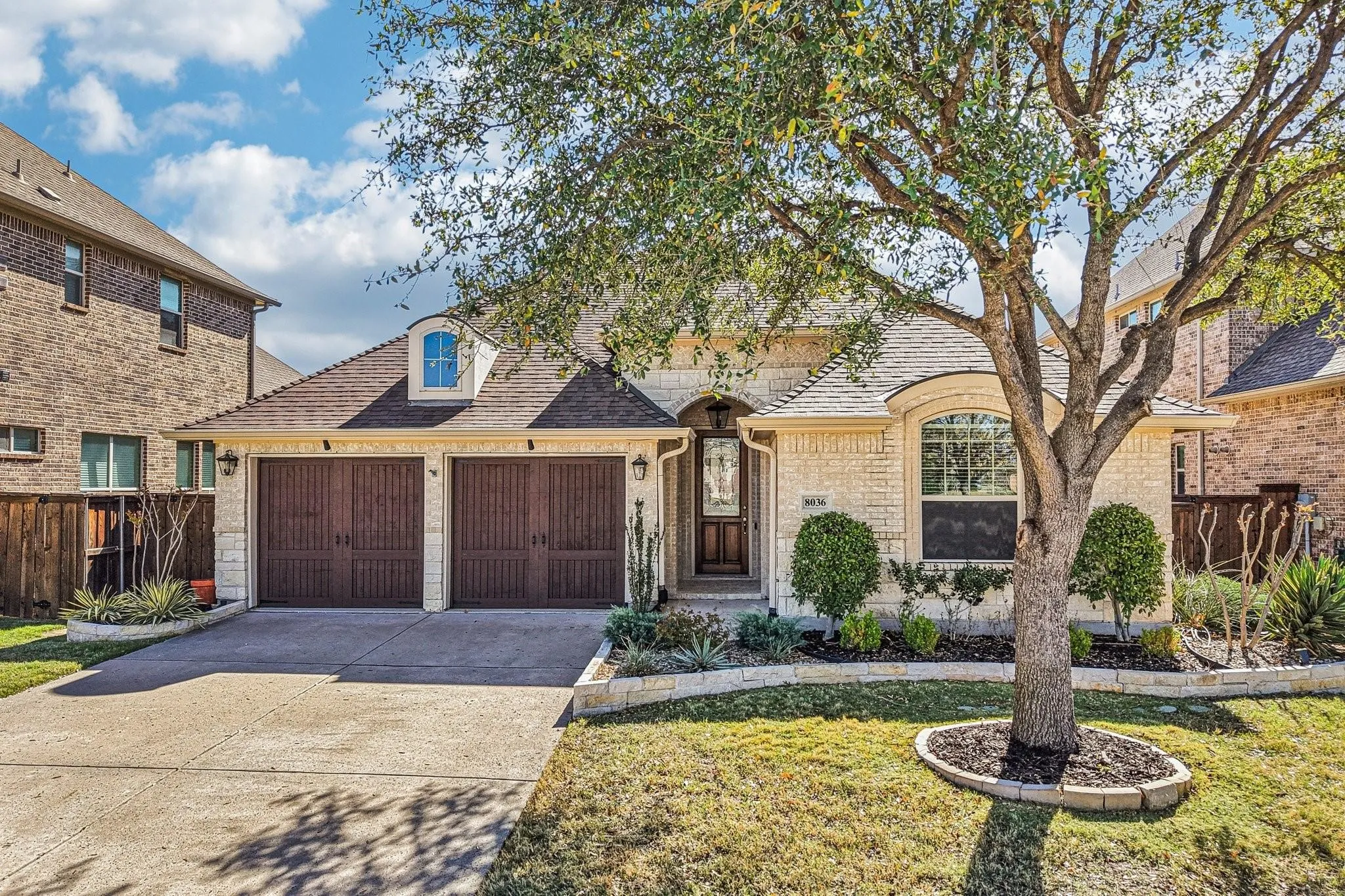 Cream brick exterior with stone accents, a two-car garage with wood-finish doors, and a concrete driveway