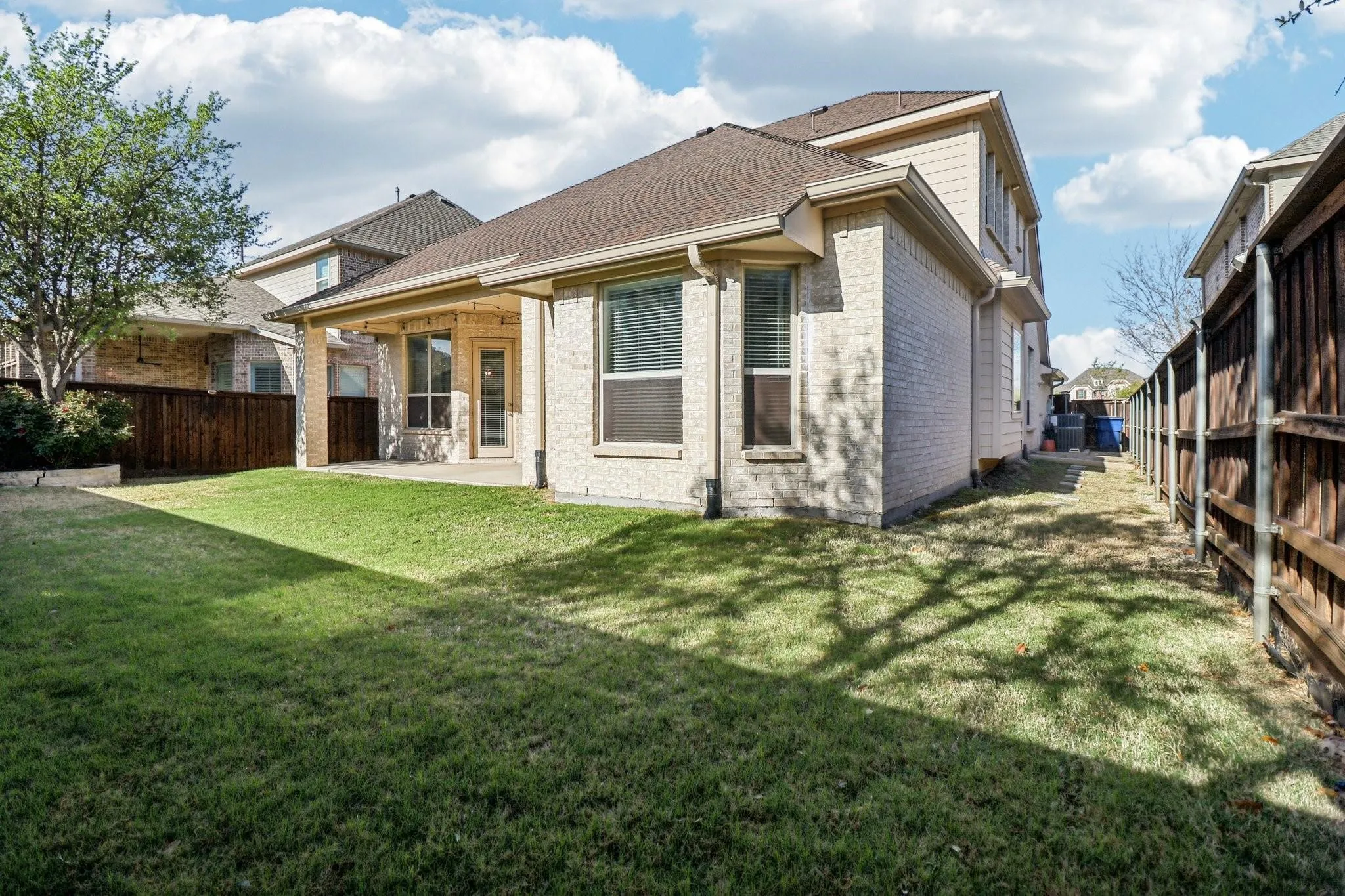 Rear exterior featuring a covered patio, brick and siding facade, and a fenced yard with mature trees