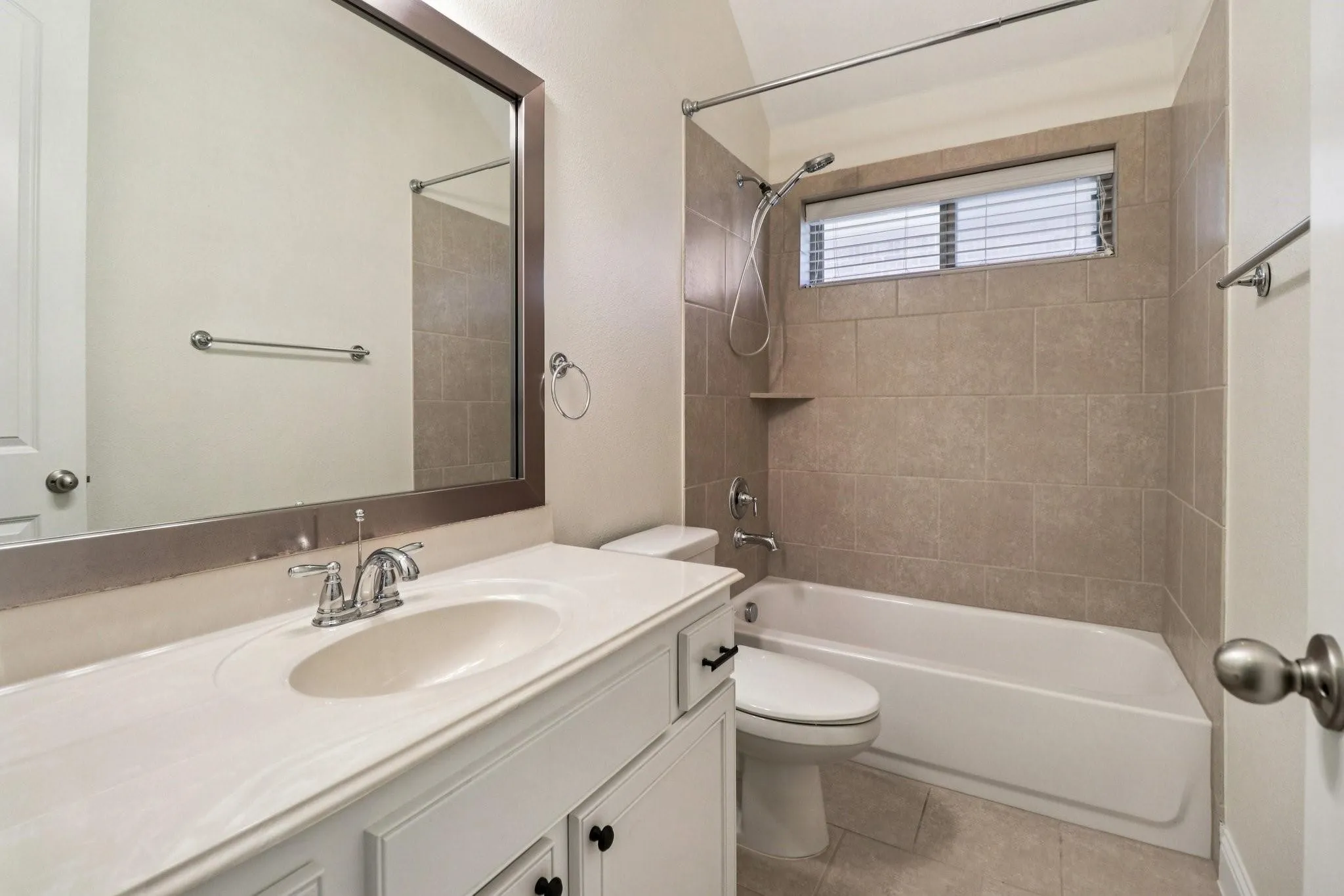 Full bathroom featuring a white vanity with integrated sink, chrome faucet, framed mirror, and a tiled shower/tub combination with a window