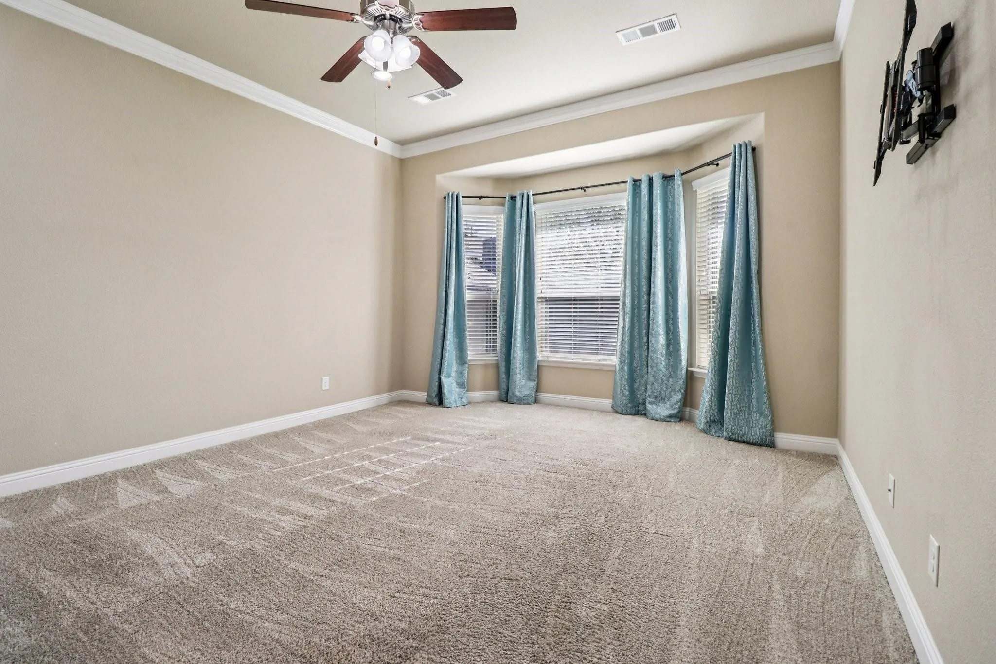 Recessed bay window with blinds and drapes, crown molding, ceiling fan with integrated lighting, neutral wall tones, and carpet flooring