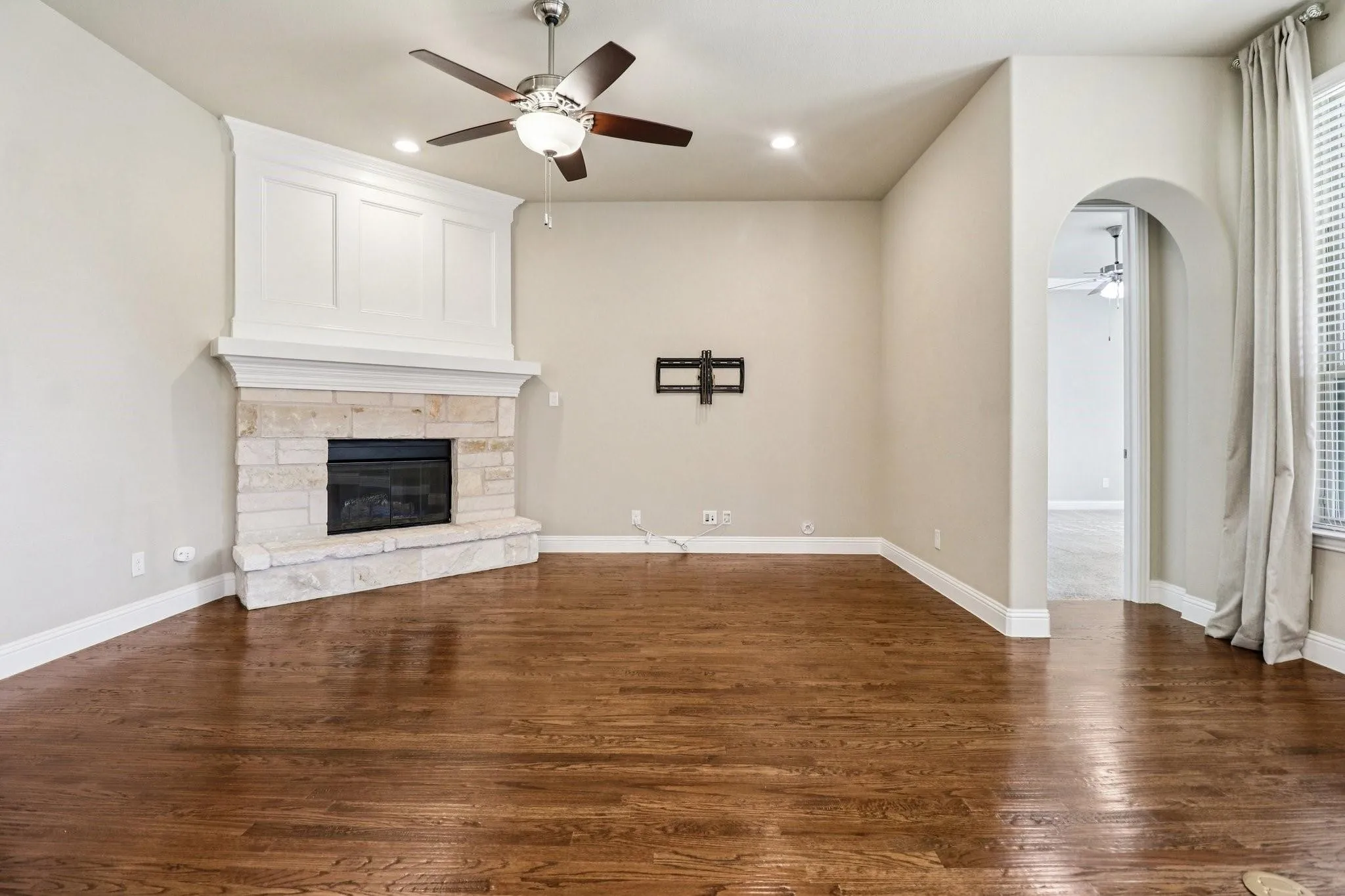 Living area featuring a stone fireplace with a white wood mantel, dark wood-finish flooring, a ceiling fan with integrated lighting, recessed ceiling lights, and an arched doorway