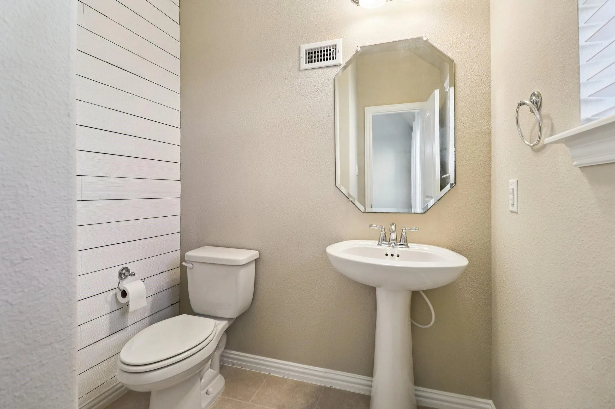 Pedestal sink with chrome fixtures and an octagonal mirror