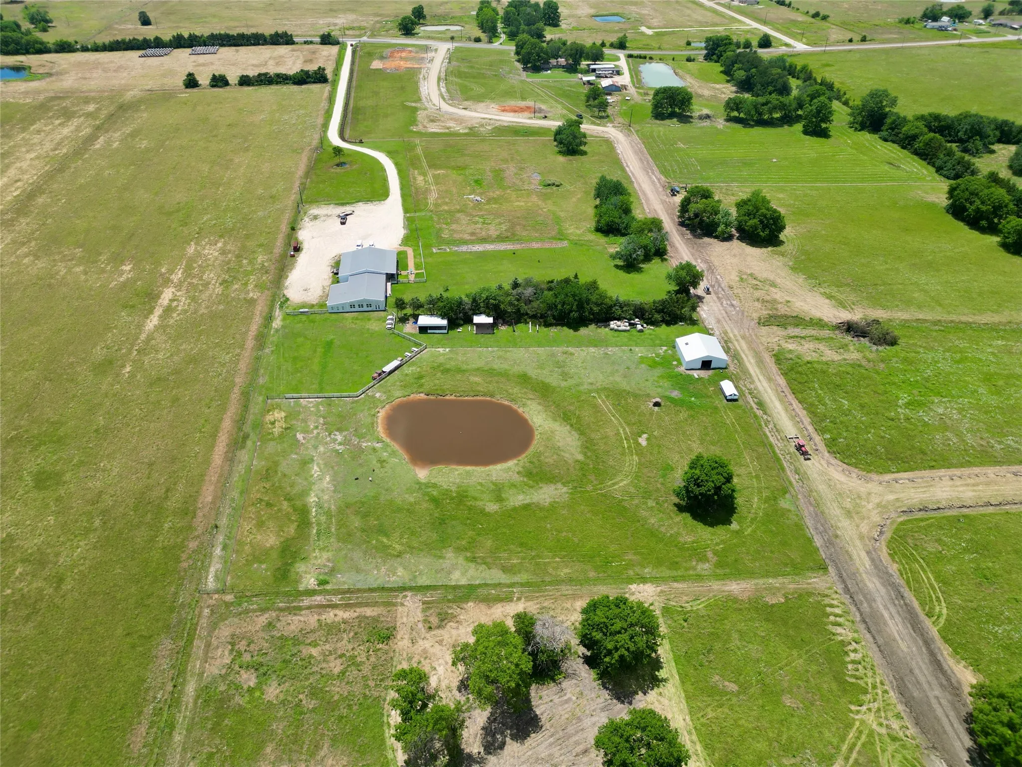 Expansive acreage featuring a private pond, a large metal-roofed structure, secondary outbuildings, and a gravel driveway