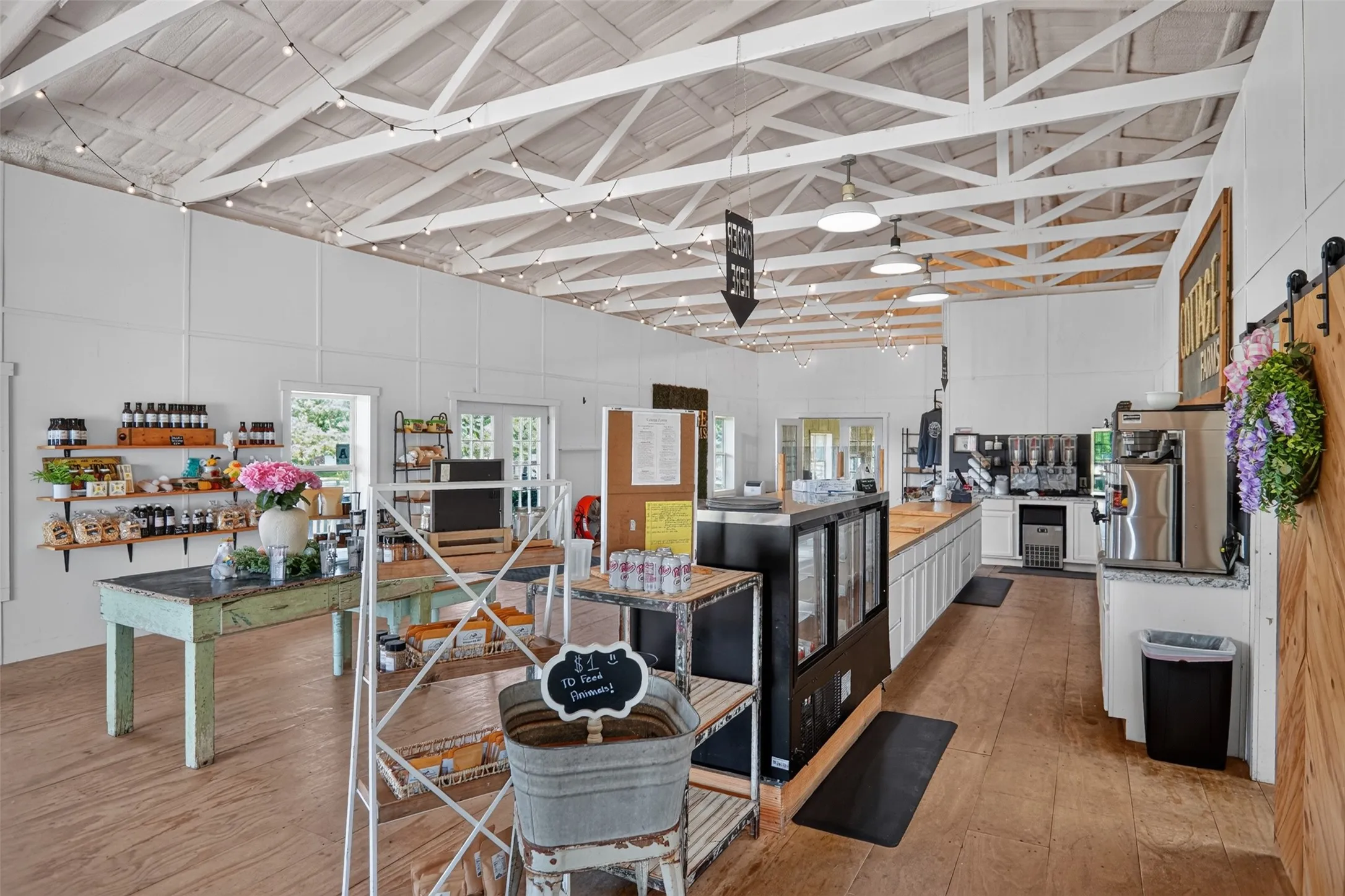 Spacious commercial interior featuring exposed white-painted ceiling trusses and wood-finish flooring