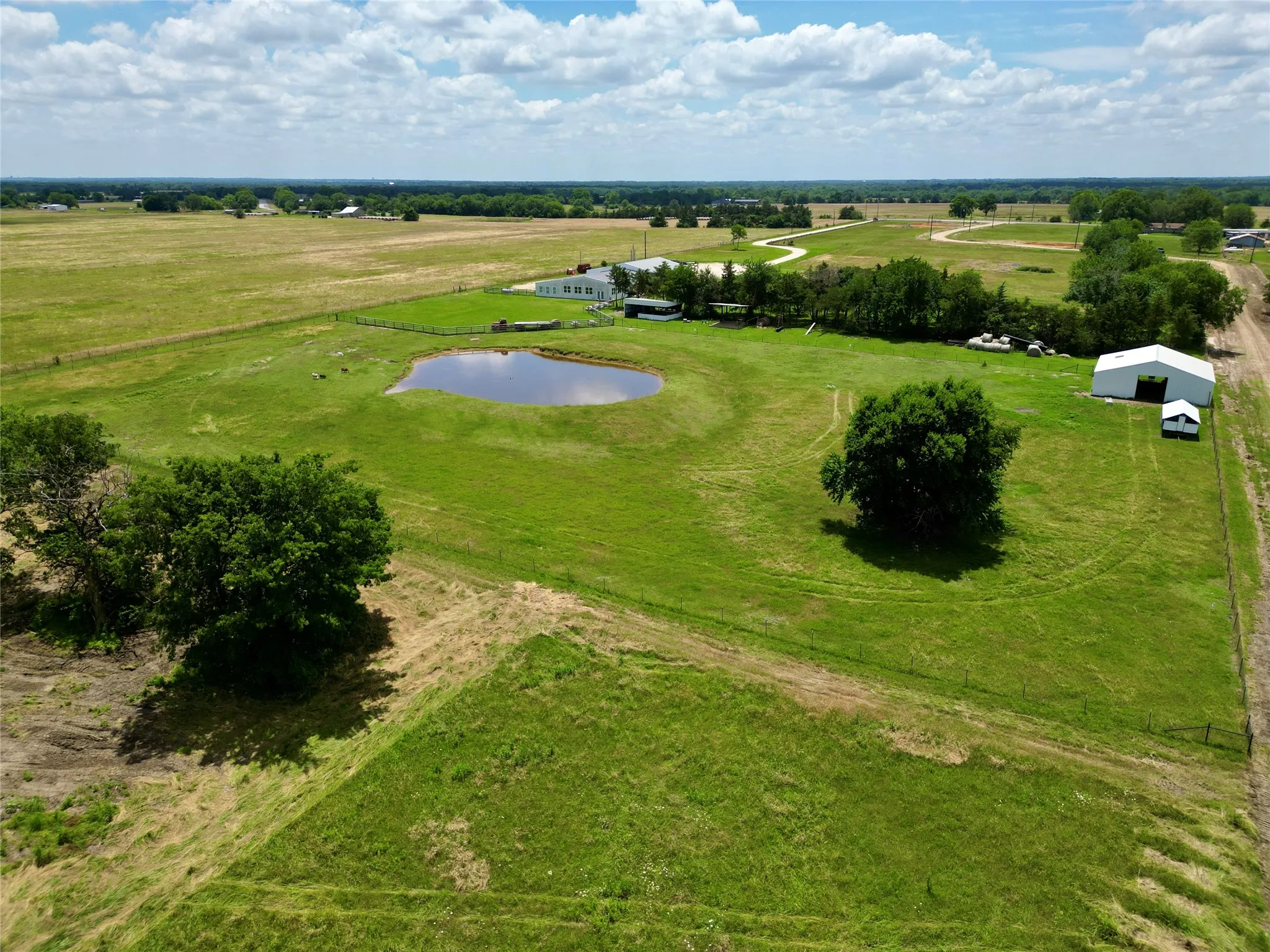 Expansive green acreage featuring a serene pond, multiple outbuildings, and scattered mature trees