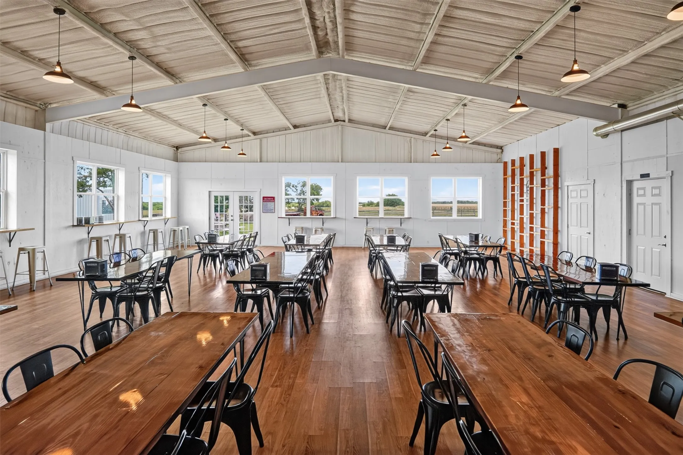 Spacious open-concept interior featuring light wood-finish flooring, white paneled walls, and a vaulted ceiling with exposed beams