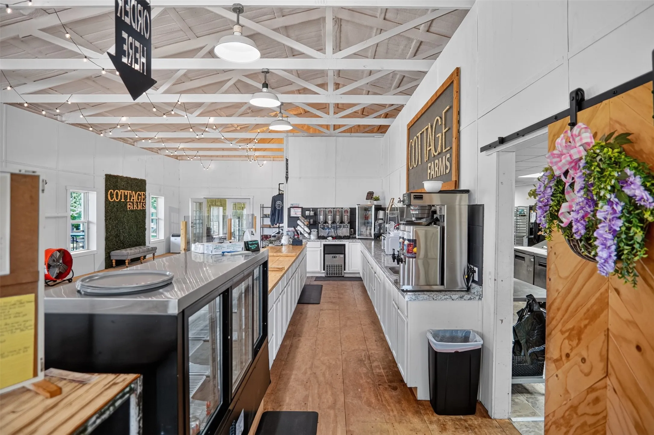 Bright commercial space featuring exposed ceiling trusses, wood-finish flooring, and white paneled walls