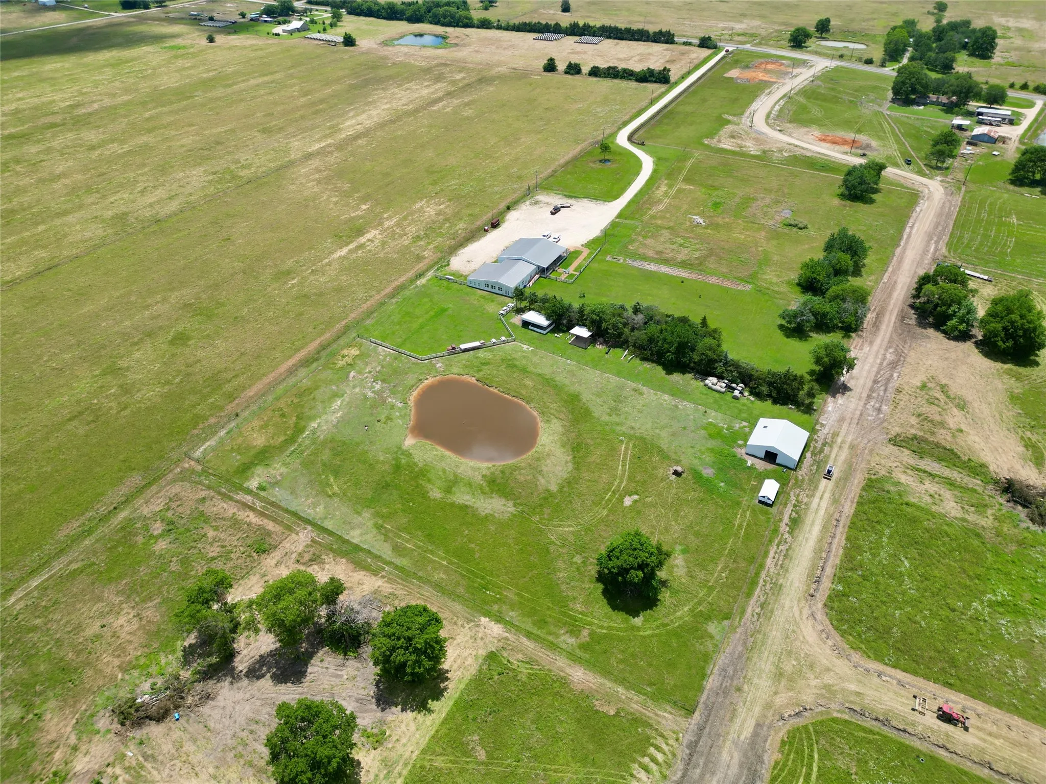 Expansive agricultural property featuring a central pond, multiple outbuildings, and a main structure with a light-colored roof