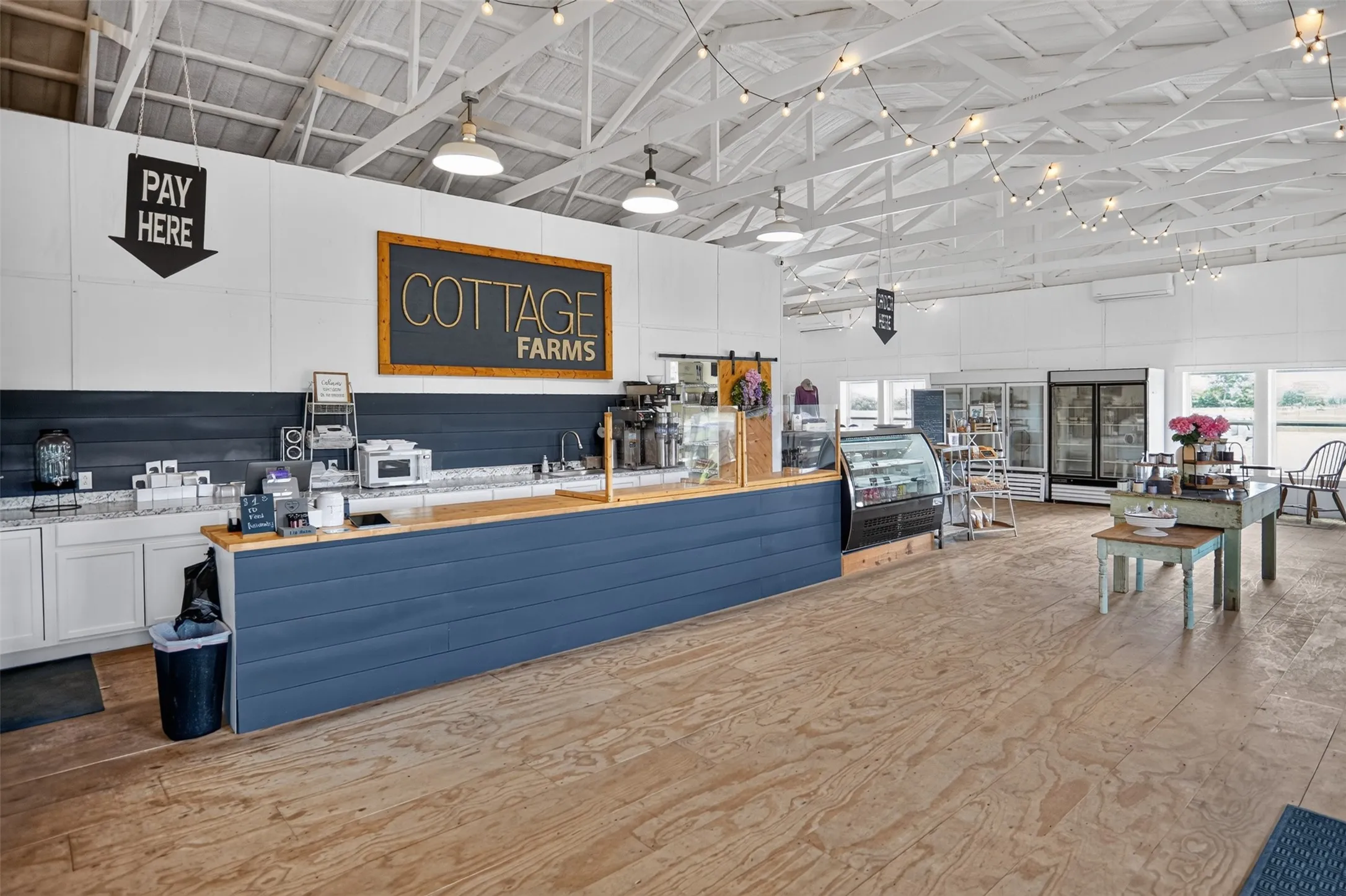 Spacious commercial interior featuring exposed white-painted ceiling trusses and wood-finish flooring