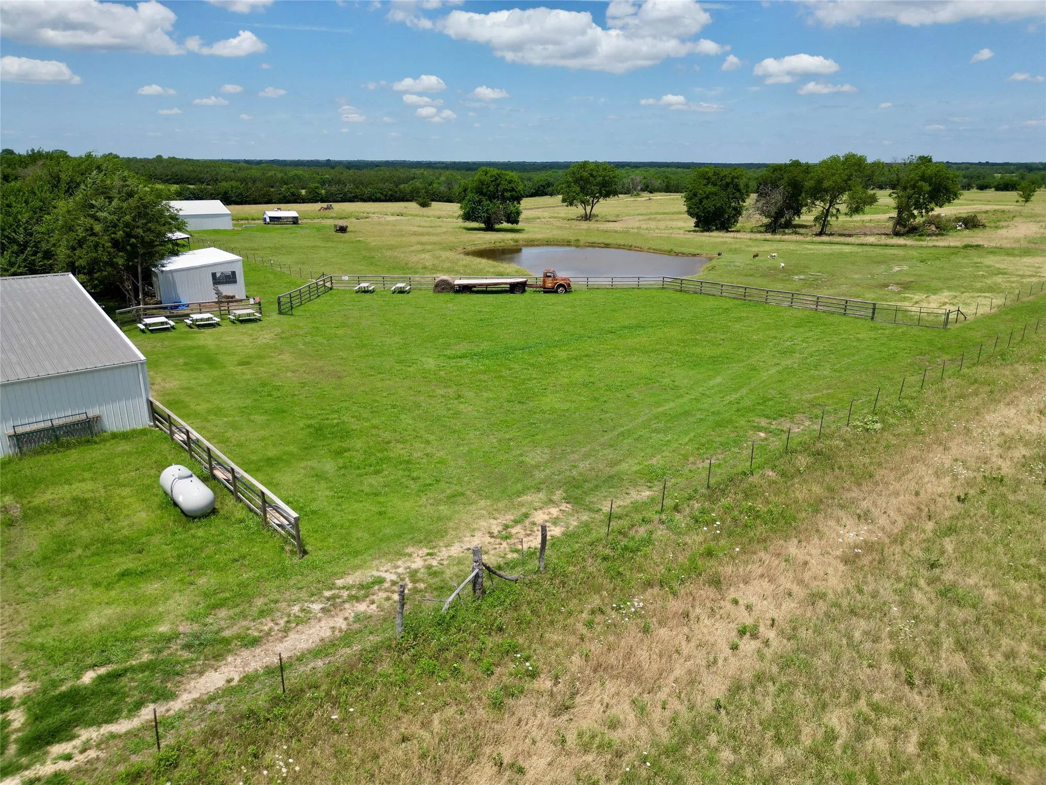 Expansive green acreage featuring multiple outbuildings, a pond, and perimeter fencing