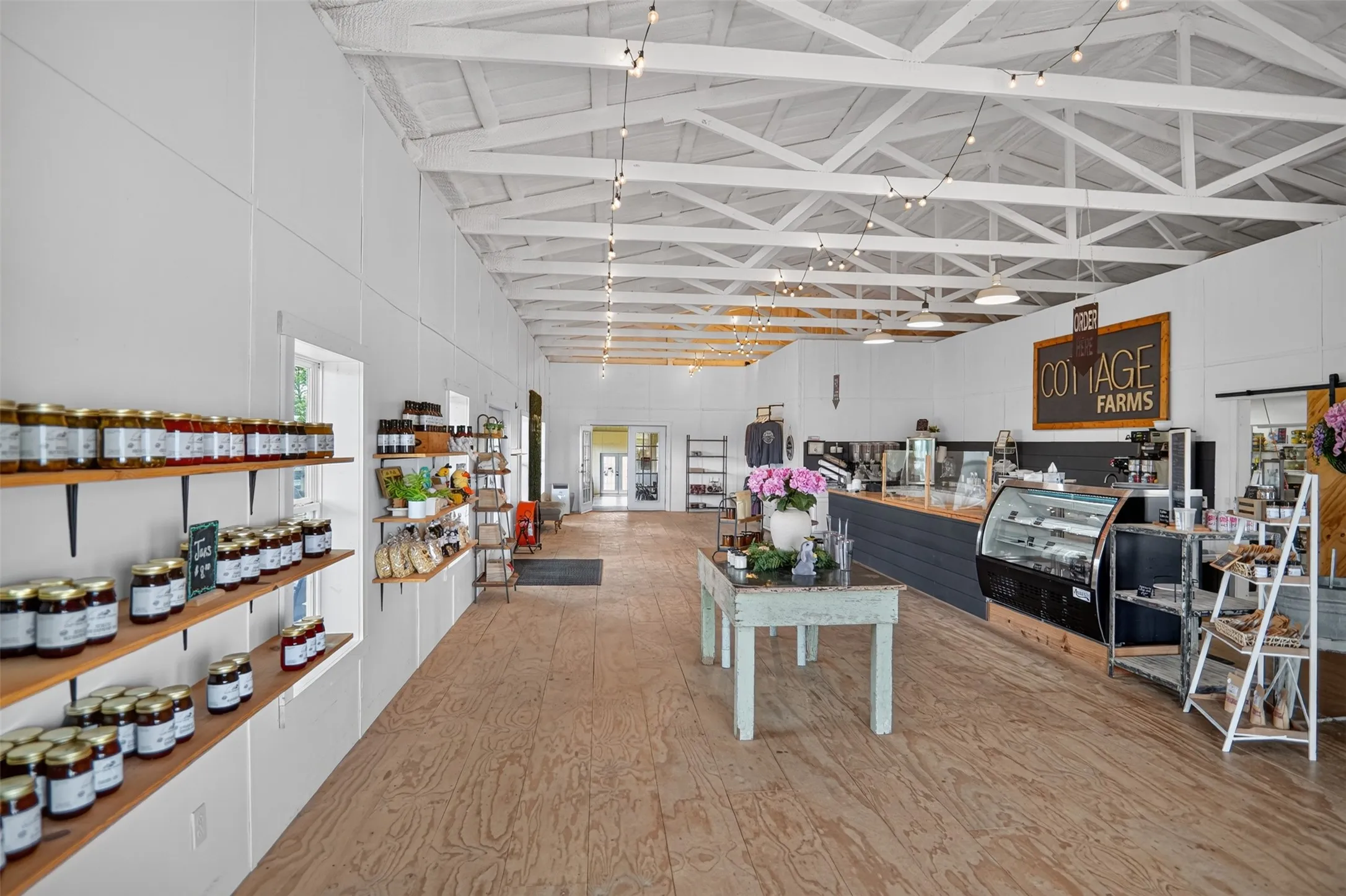 Spacious commercial interior featuring exposed white-painted ceiling trusses, light wood-finish flooring, and bright white walls