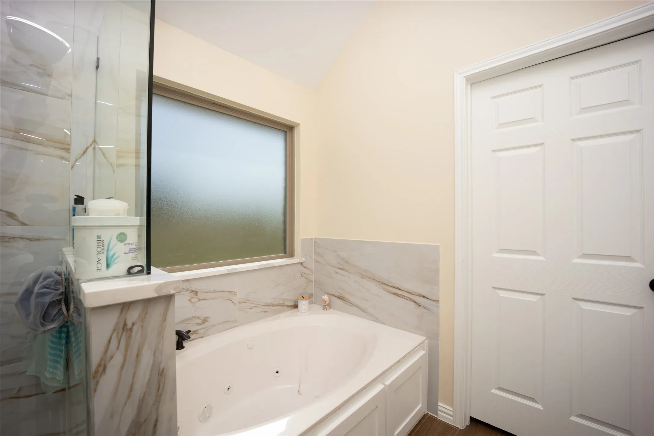Soaking tub with integrated jets, surrounded by marble-look tile and a frosted window