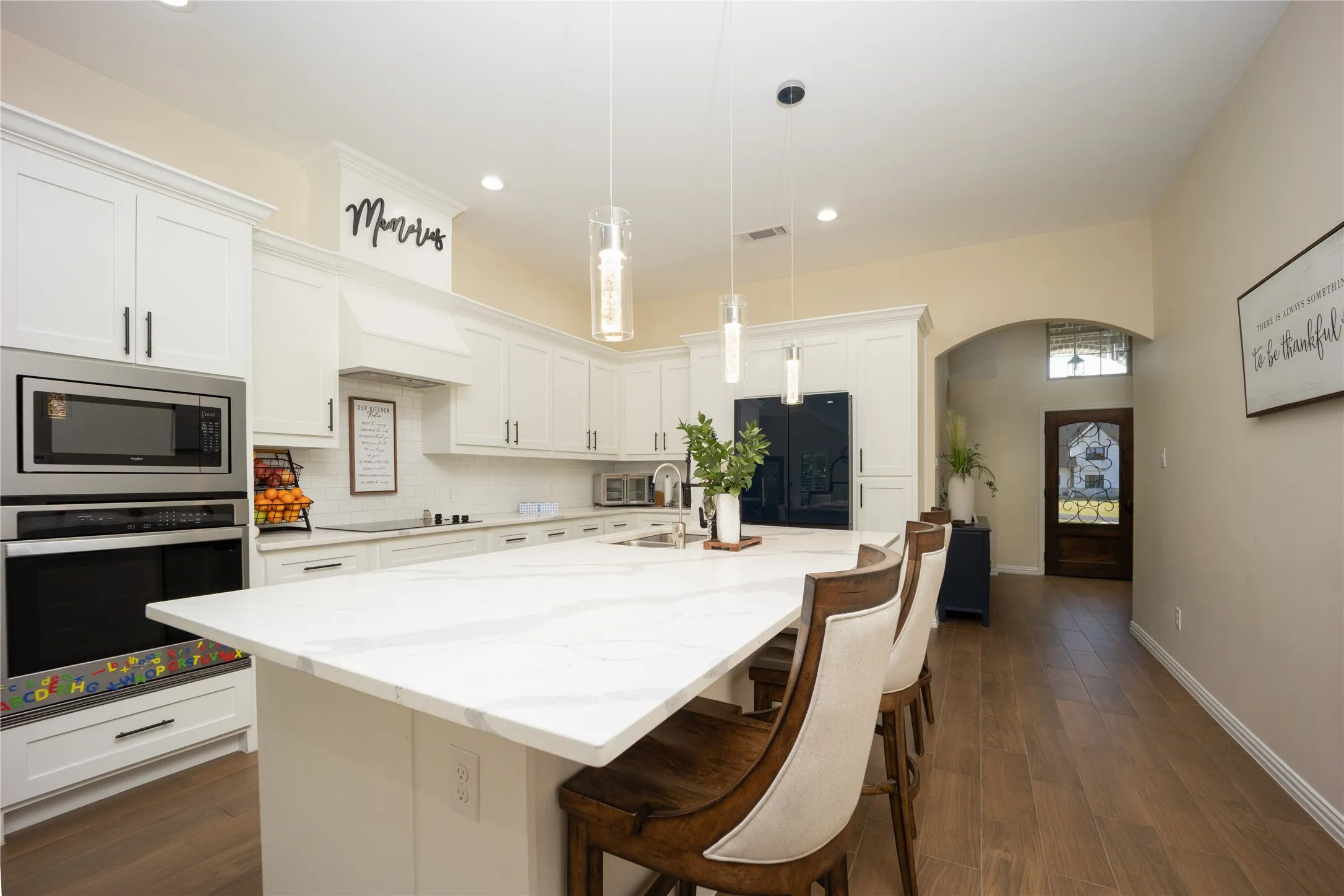 Spacious kitchen featuring an expansive island with seating, white shaker cabinetry, stainless steel appliances, and wood-finish flooring