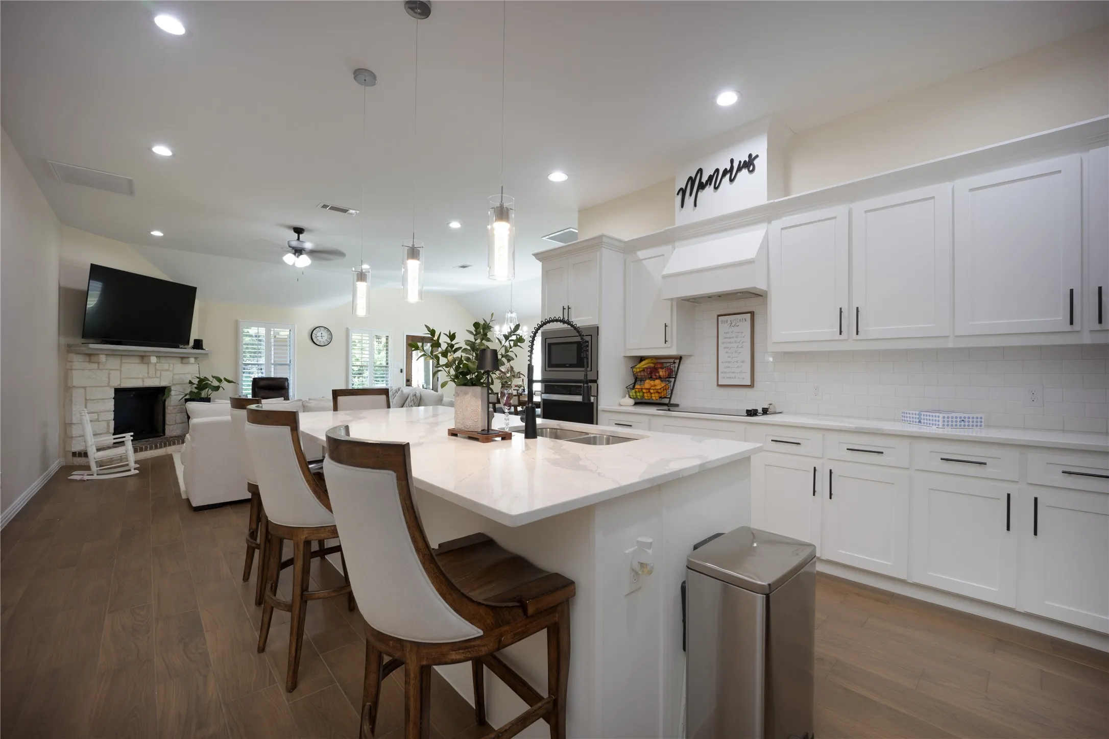 Gourmet kitchen featuring a large island with a waterfall-edge countertop, pendant lighting, shaker-style cabinetry, a white subway tile backsplash, and built-in stainless steel appliances