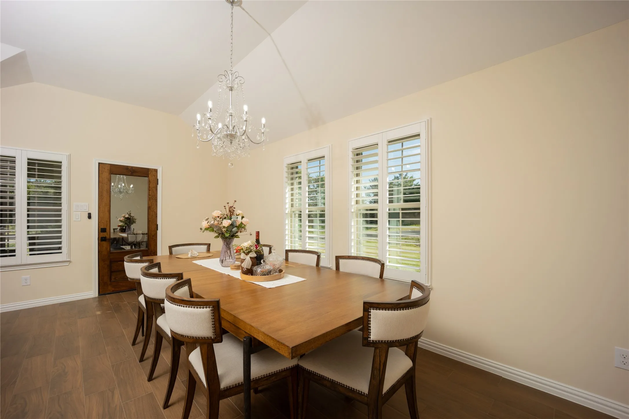 Vaulted ceiling dining area featuring wood-finish flooring, multiple windows with white shutters, and a crystal chandelier