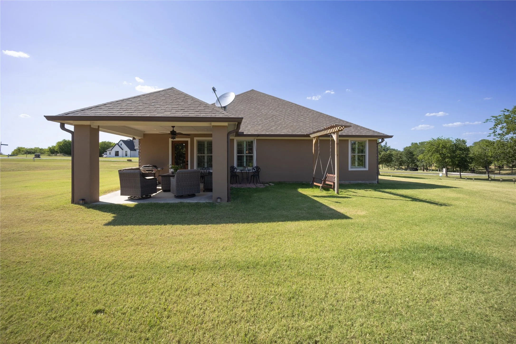 Expansive green lawn surrounds a rear elevation featuring a covered patio with a ceiling fan, a swing structure, and multiple windows