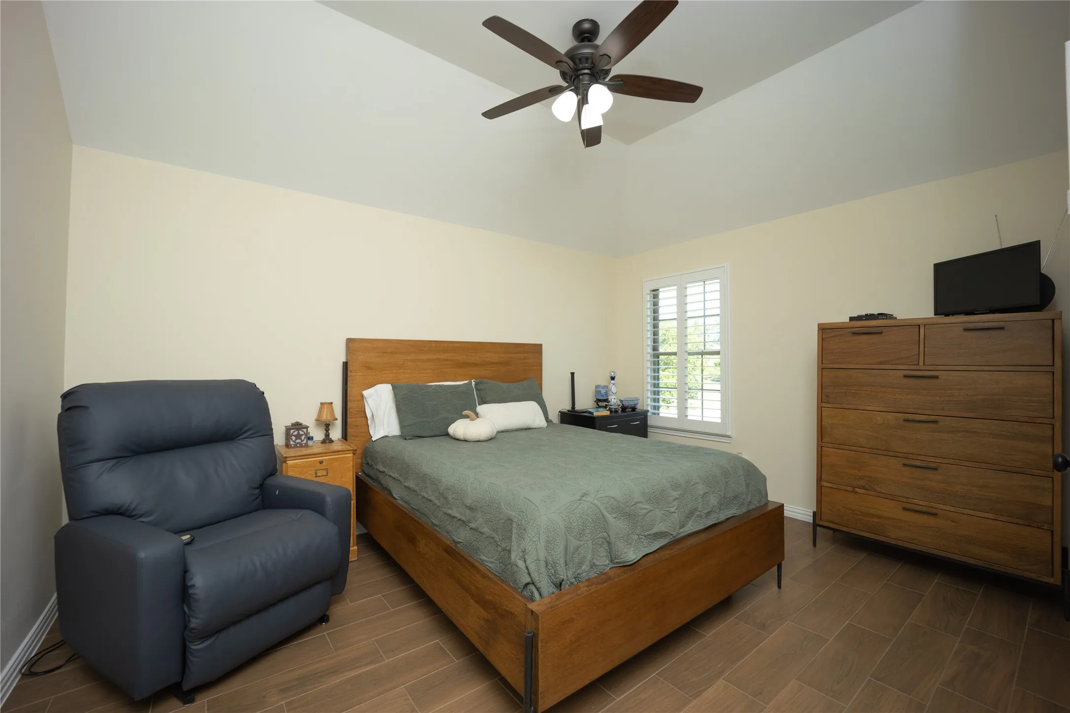 Bedroom featuring vaulted ceilings, wood-finish flooring, a ceiling fan with light kit, and a window with plantation shutters