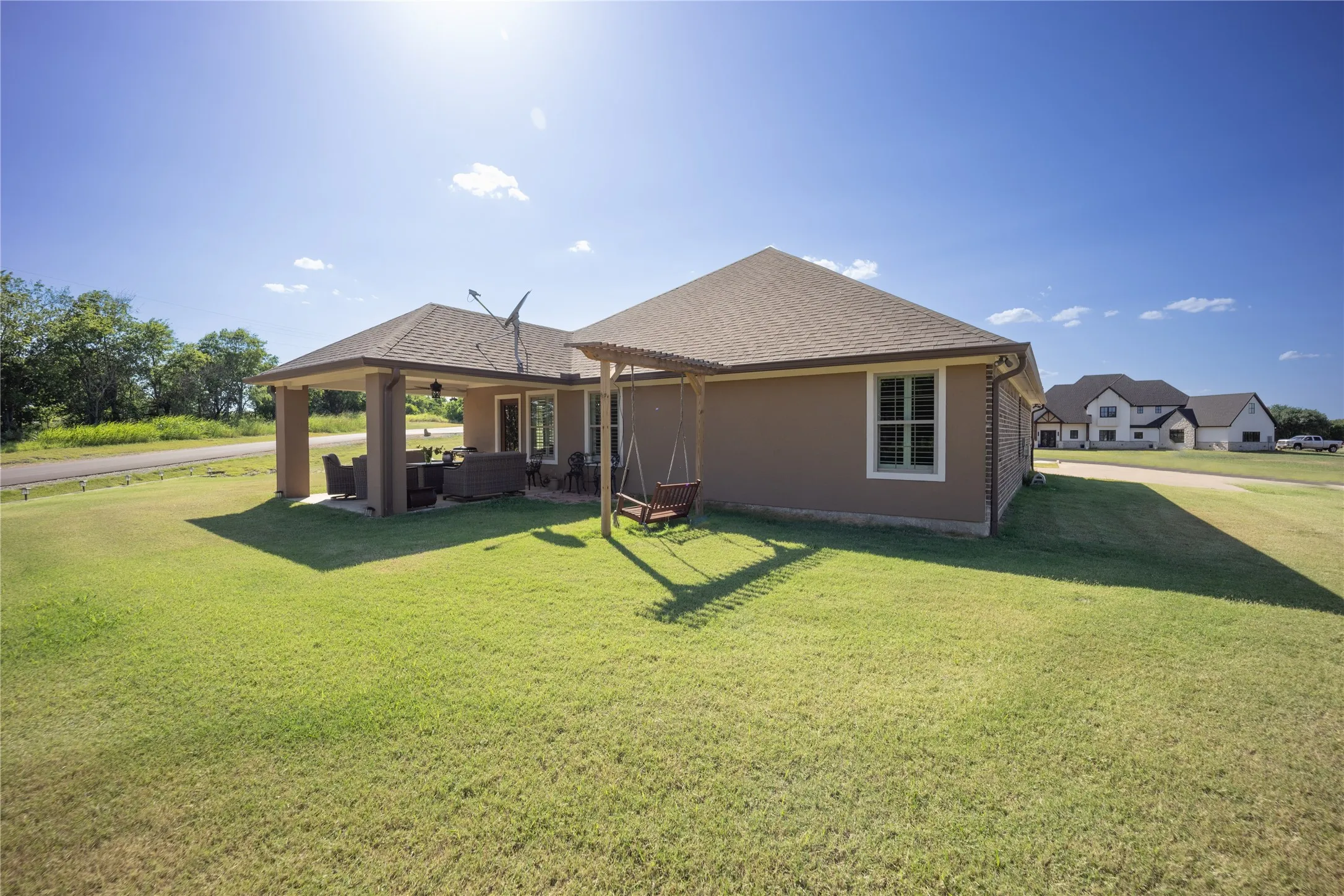 Expansive green lawn surrounds this property featuring a covered patio, a secondary covered outdoor sitting area, and a window with louvered shutters