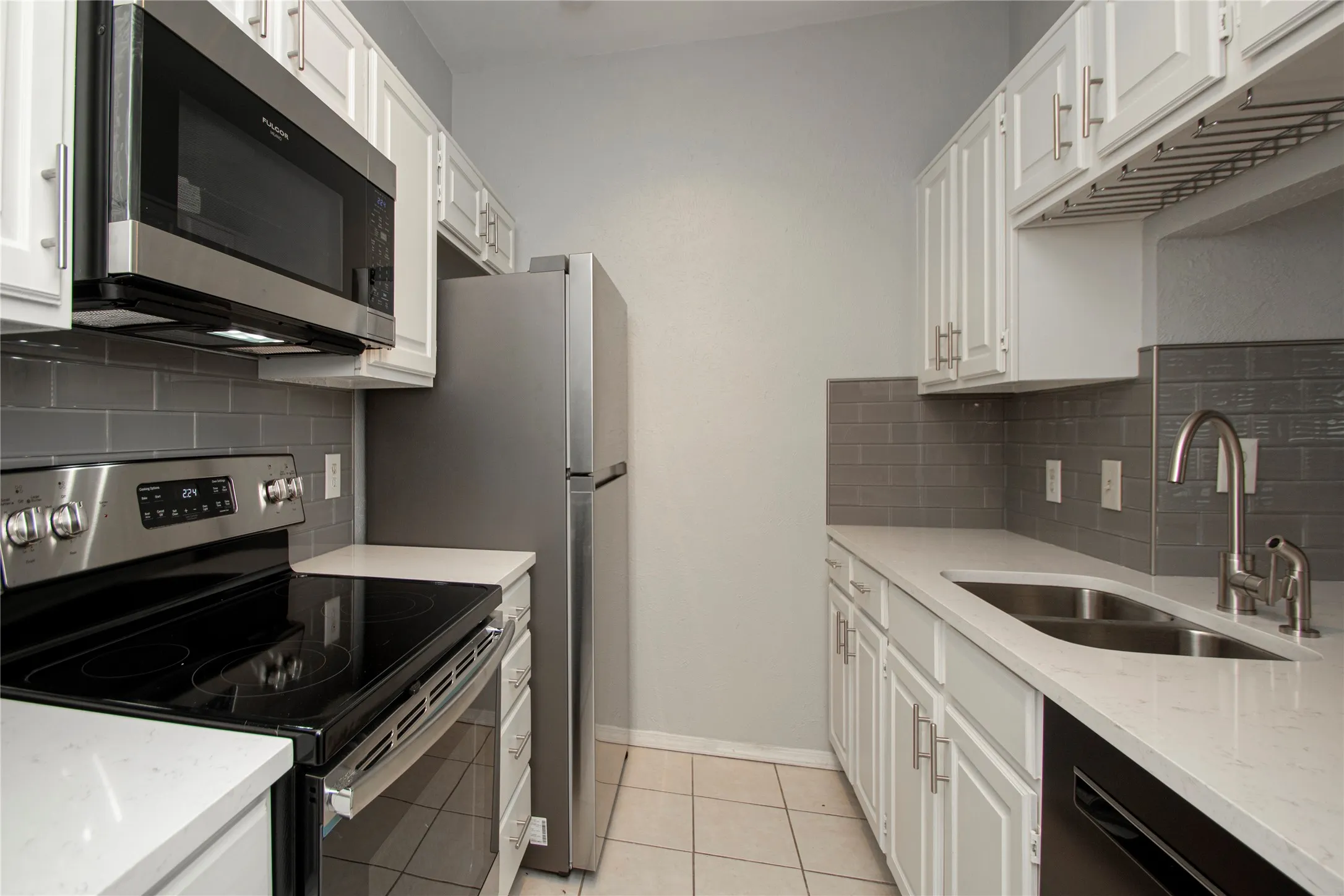 Updated kitchen featuring white shaker cabinetry, stainless steel appliances, light-toned countertops, and a gray subway tile backsplash
