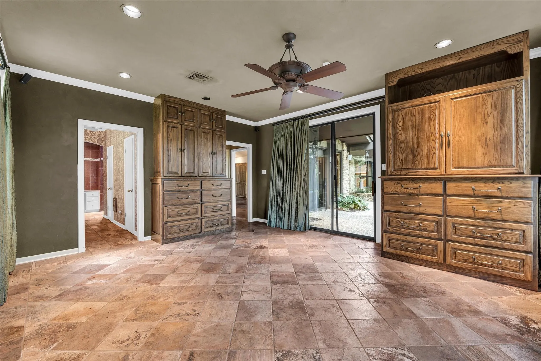 Spacious room featuring large format tile flooring, two built-in wood cabinetry units with drawers, recessed lighting, and a ceiling fan