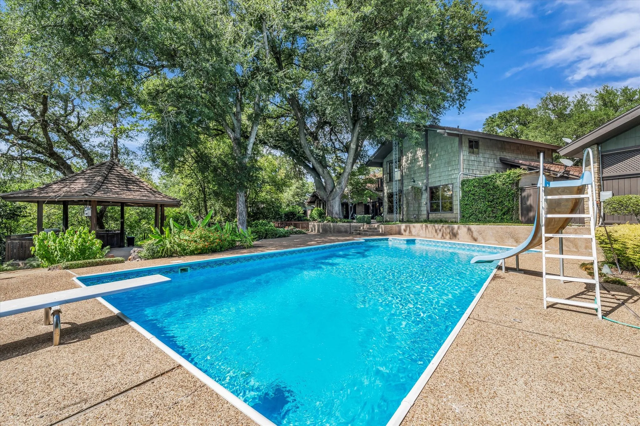 Inviting swimming pool with diving board and slide, surrounded by a textured aggregate deck