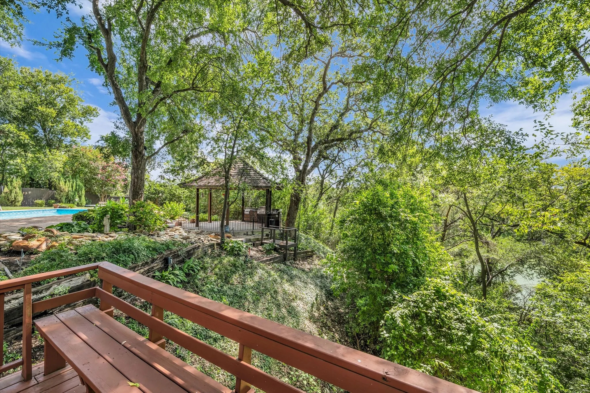 Expansive outdoor area featuring a wooden deck with built-in seating, a separate gazebo, and an in-ground swimming pool