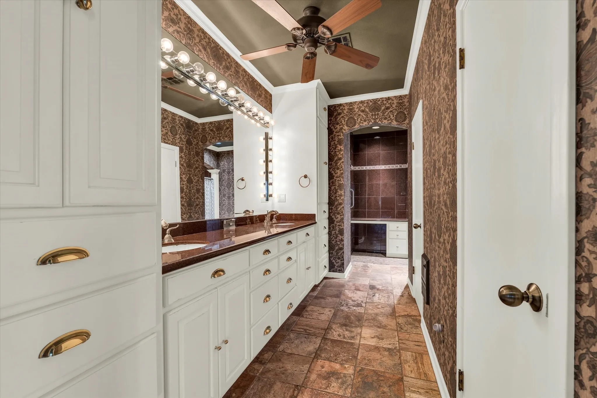 Expansive vanity featuring dual undermount sinks, rich countertop, and white cabinetry with brass hardware