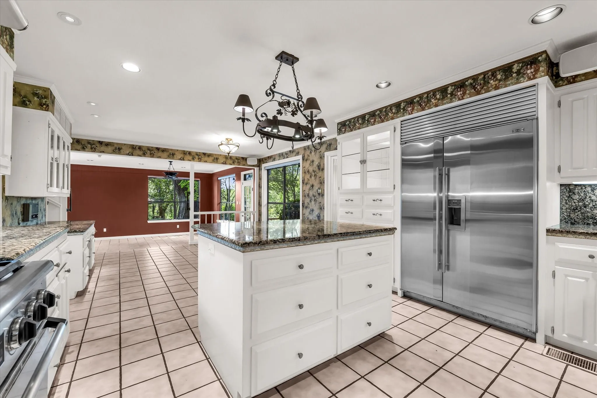 Kitchen featuring a large central island with a granite countertop, white cabinetry with display glass, stainless steel refrigerator, and tile flooring