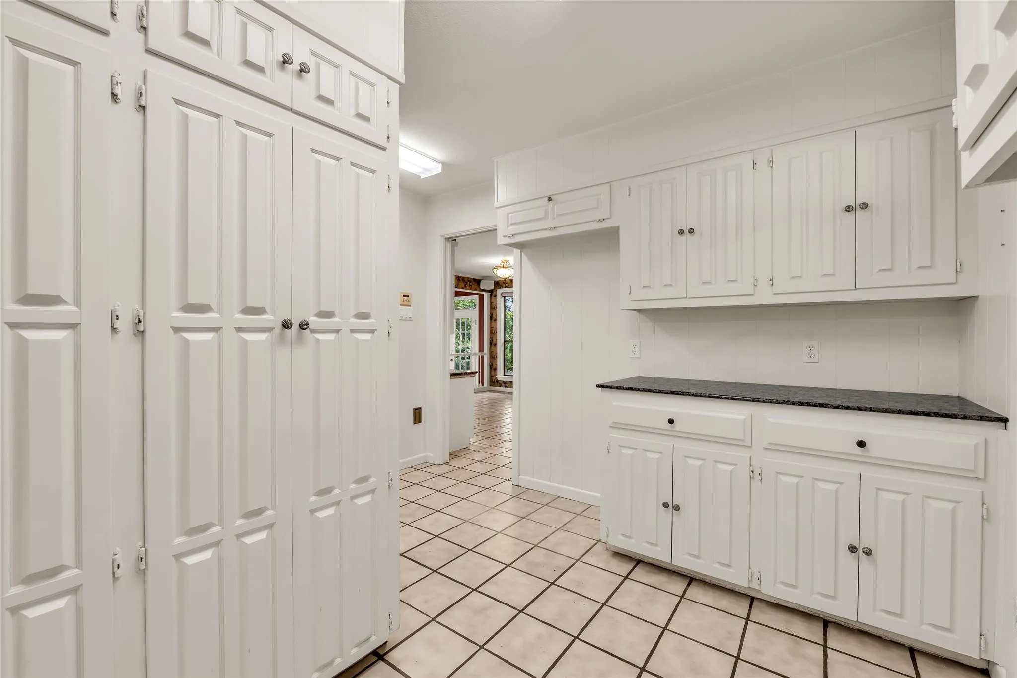 Kitchen featuring extensive white cabinetry, dark countertops, and ceramic tile flooring
