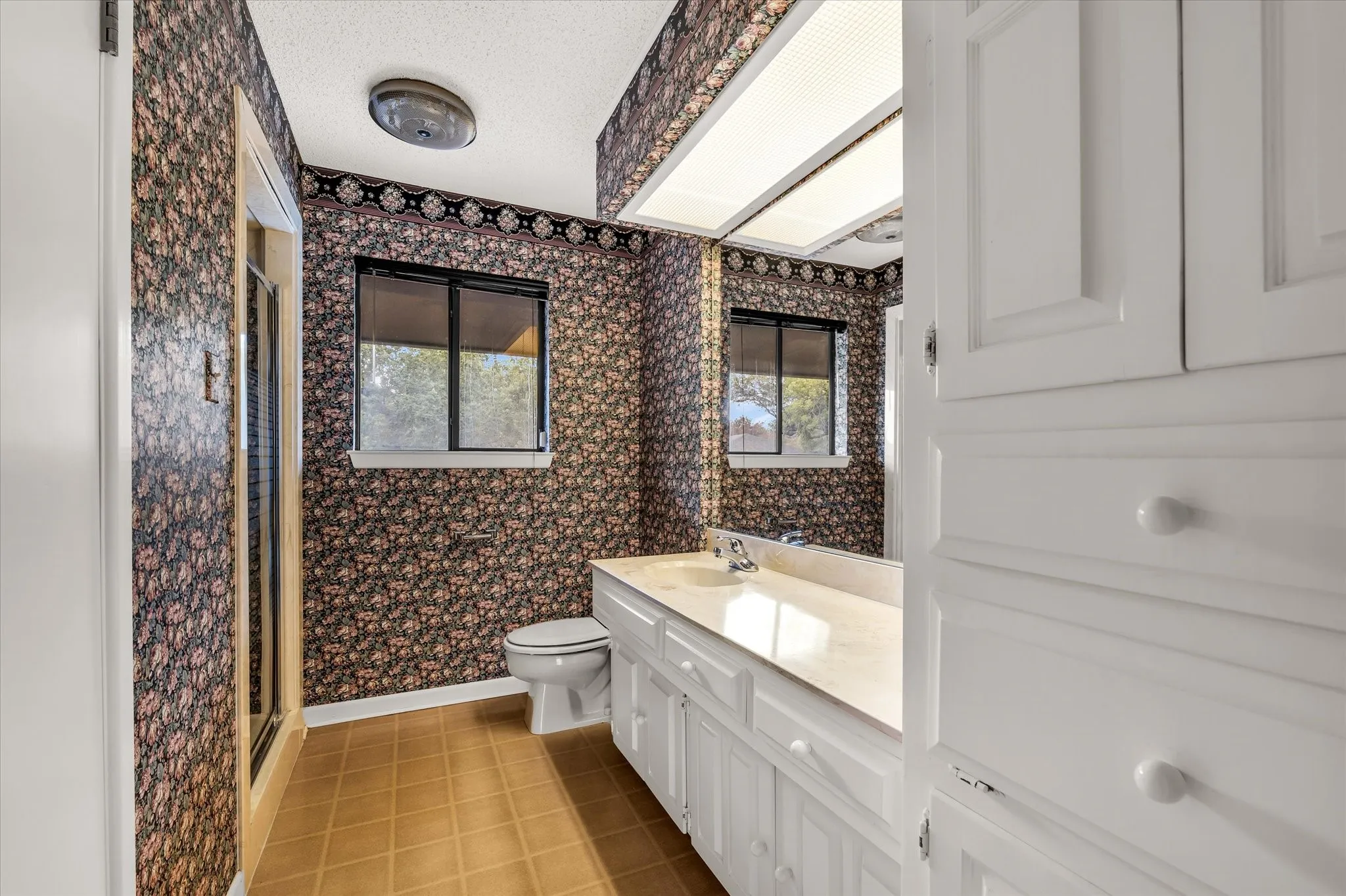 Bathroom featuring patterned wallpaper, a single vanity with a light-colored countertop, and a built-in storage cabinet with white paneled doors