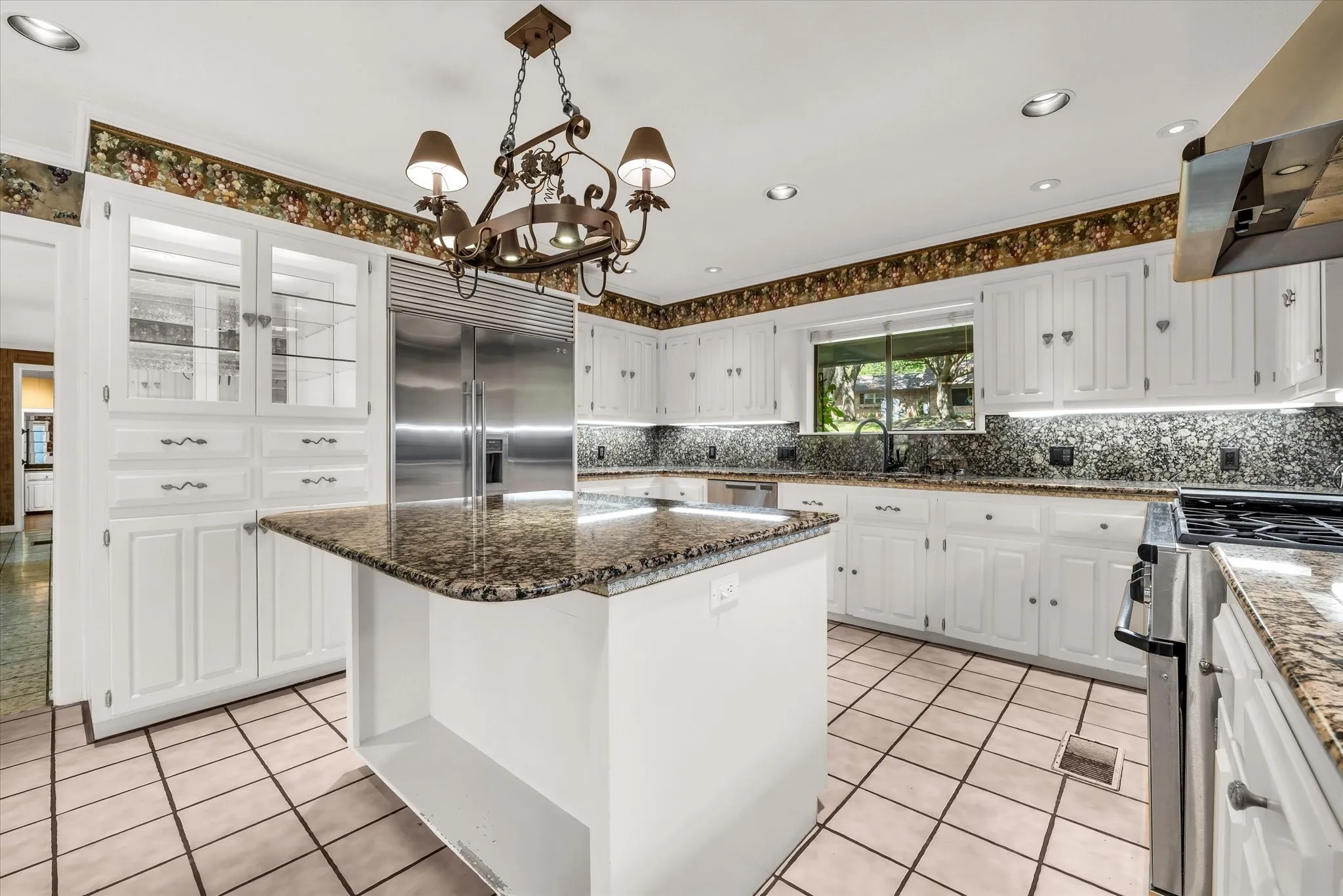 Kitchen featuring an island with a granite countertop, white cabinetry with display uppers, stainless steel refrigerator, and tile flooring