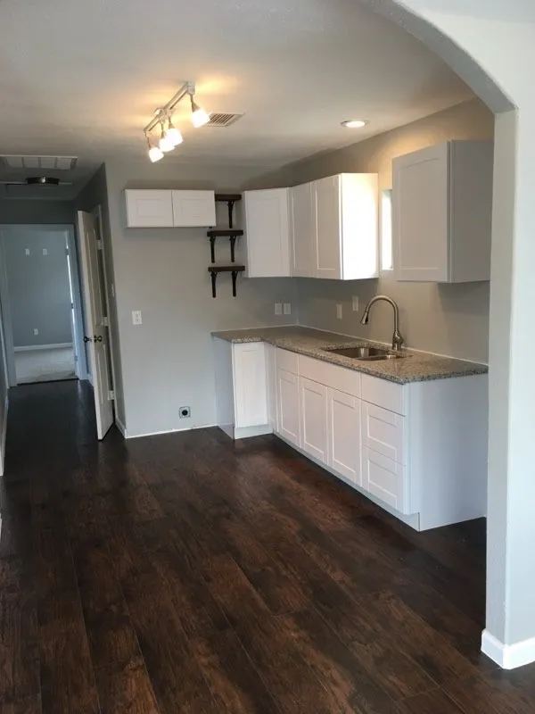 Kitchen featuring dark hardwood / wood-style flooring, rail lighting, white cabinetry, light stone countertops, and sink