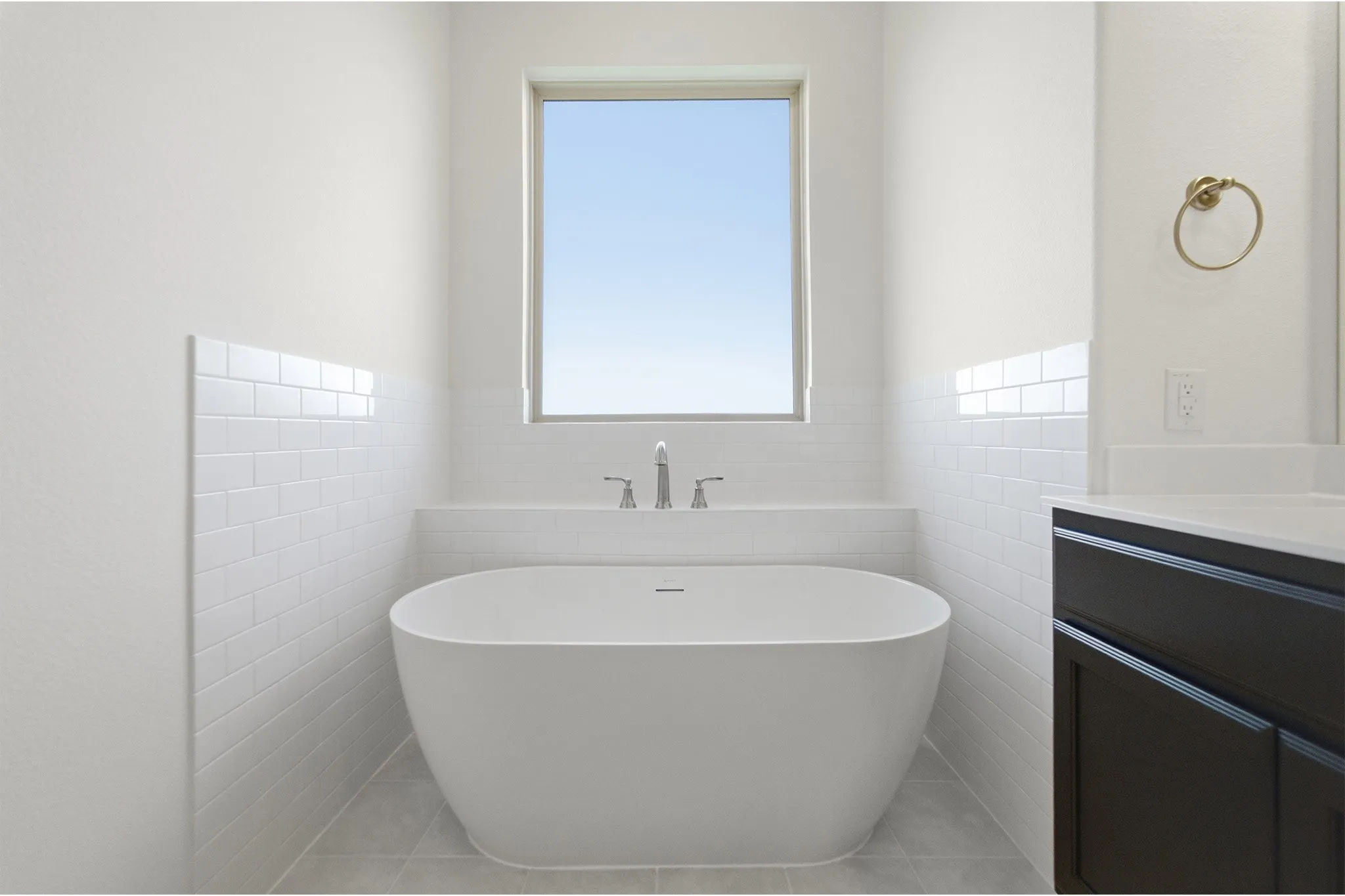 Freestanding oval soaking tub with deck-mounted chrome faucet, surrounded by white subway tile wainscoting
