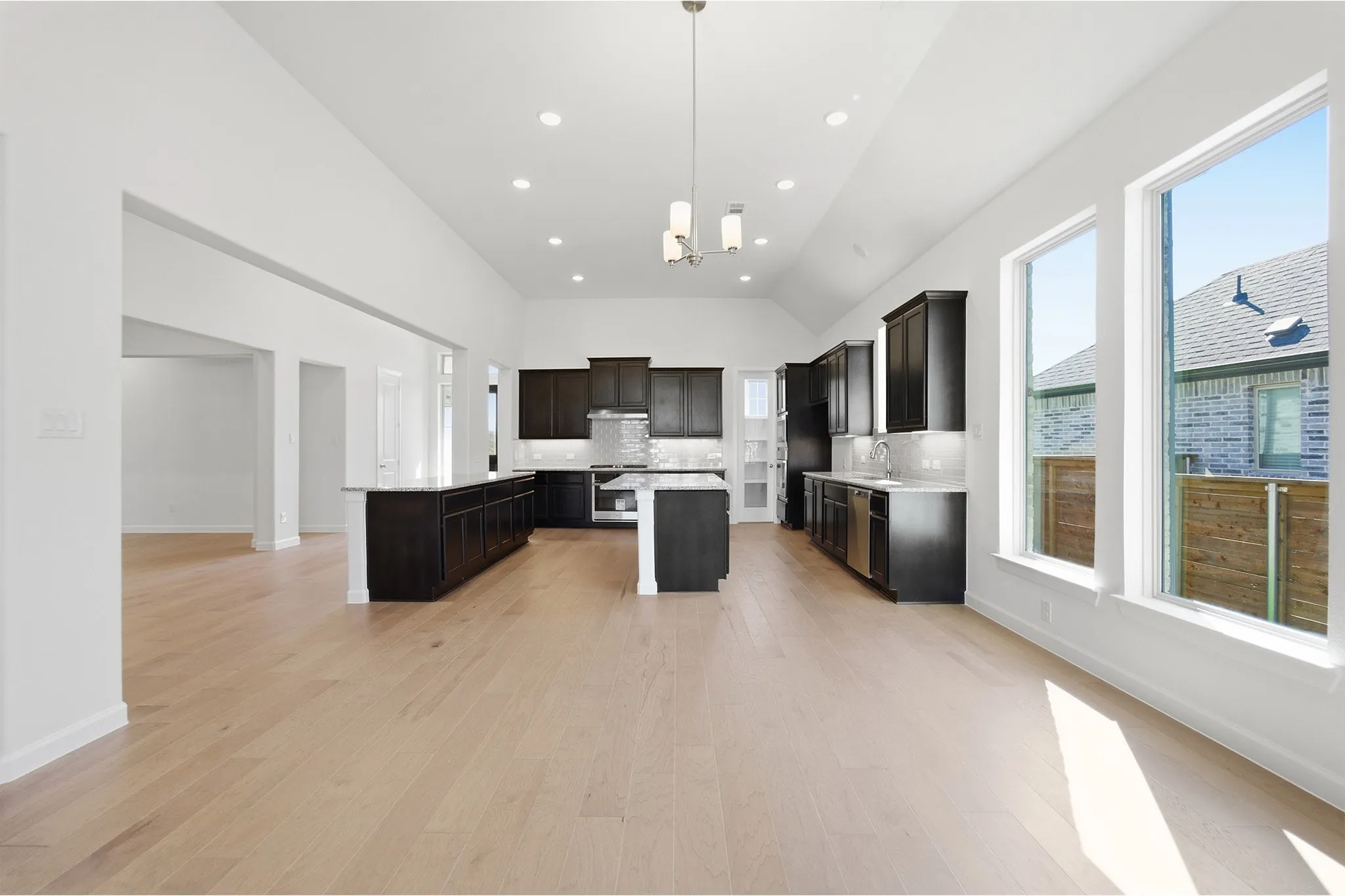 Spacious kitchen featuring dark cabinetry, two islands with countertop space, stainless steel appliances, and wood-finish flooring