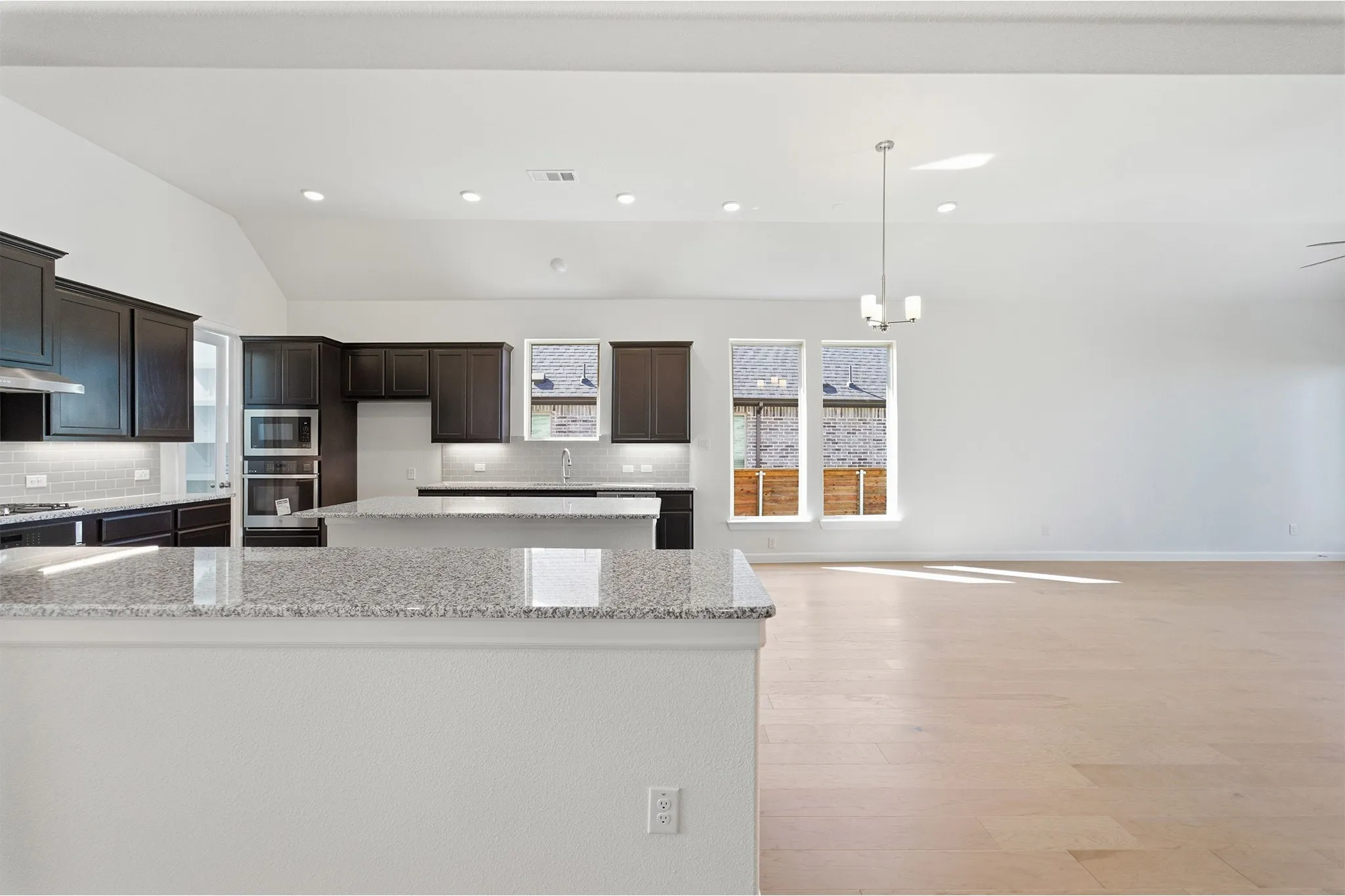 Open-concept kitchen and living area featuring granite countertops, dark wood cabinetry, stainless steel appliances, and light wood-finish flooring