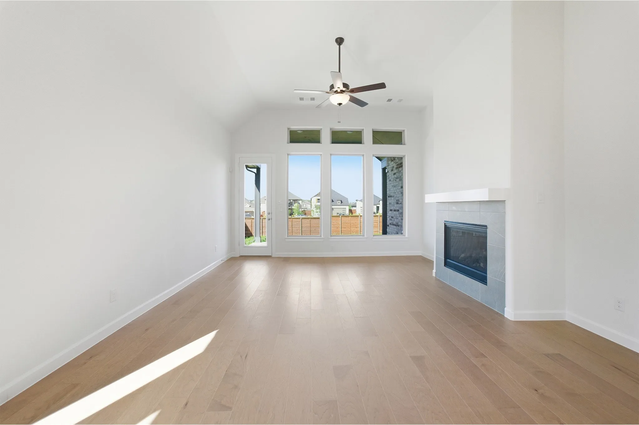 Living space featuring vaulted ceilings, wood-finish flooring, a contemporary fireplace with tile surround, a ceiling fan, and large windows with transom accents