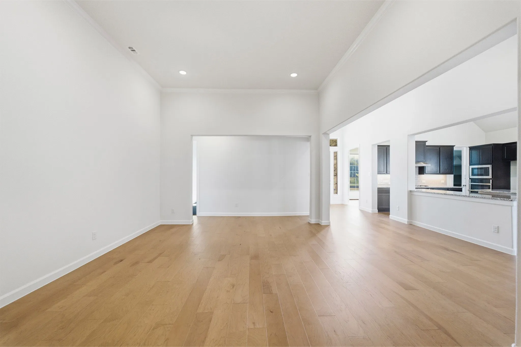 Open-concept living space featuring light wood-finish flooring, recessed lighting, and crisp white walls