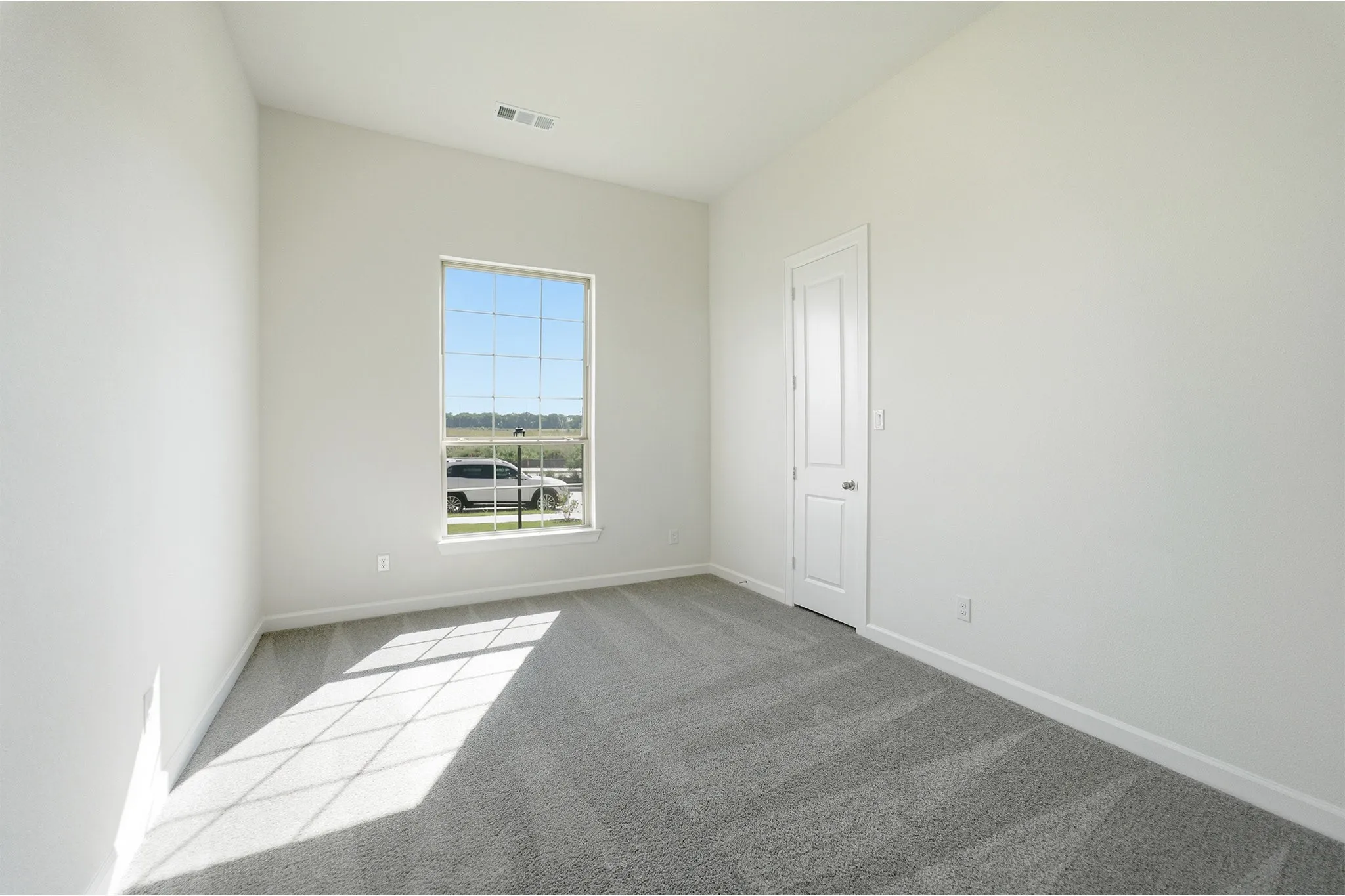 Spacious room featuring a large window, light gray carpet, white walls, and a white interior door
